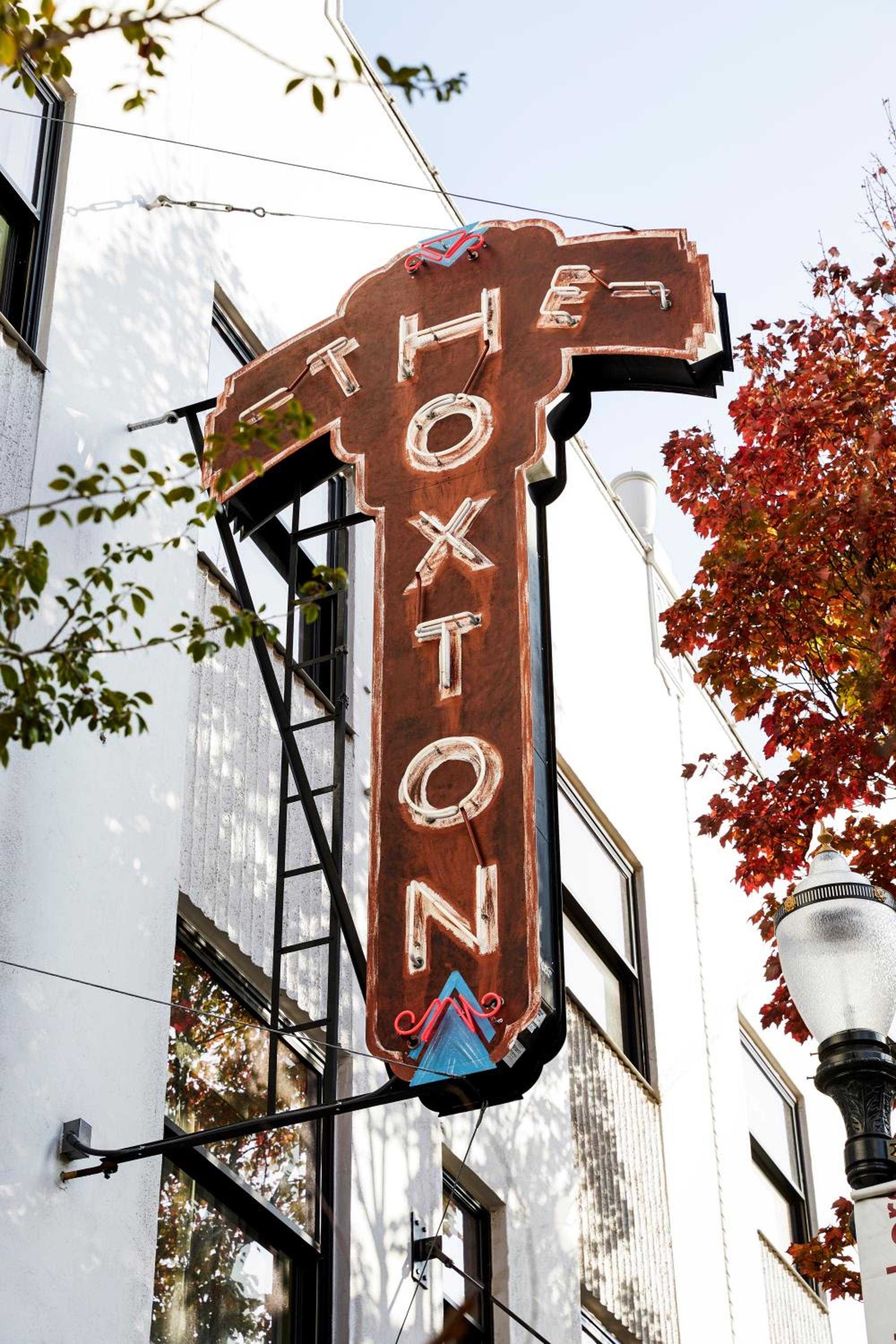 Vintage neon letters spell out the hotel's identity against weathered brick, while autumn maples frame this charming Portland street corner with nostalgic warmth.
