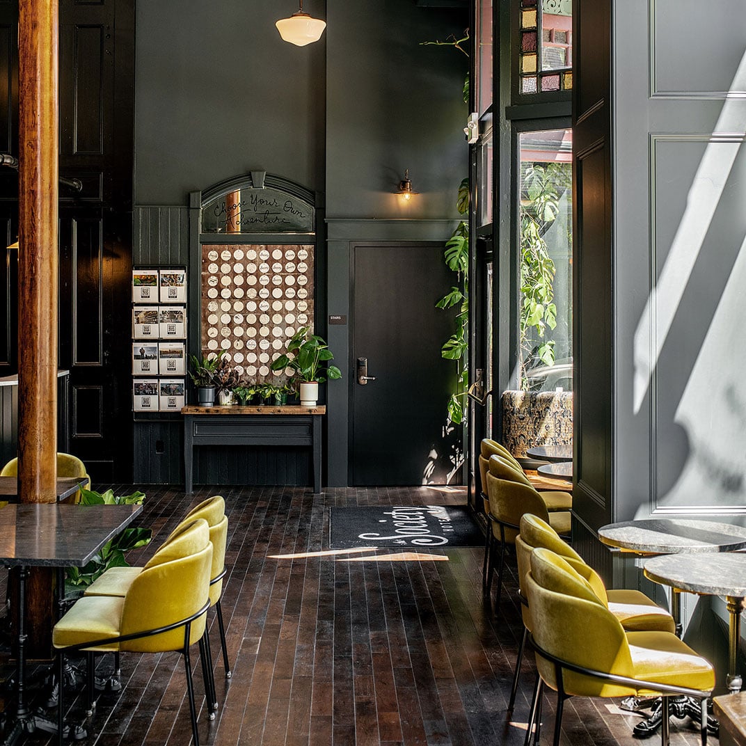 Moody charcoal walls frame vintage mustard velvet chairs and an eclectic coffee display, where industrial pendant lights cast intimate shadows across reclaimed wood floors.