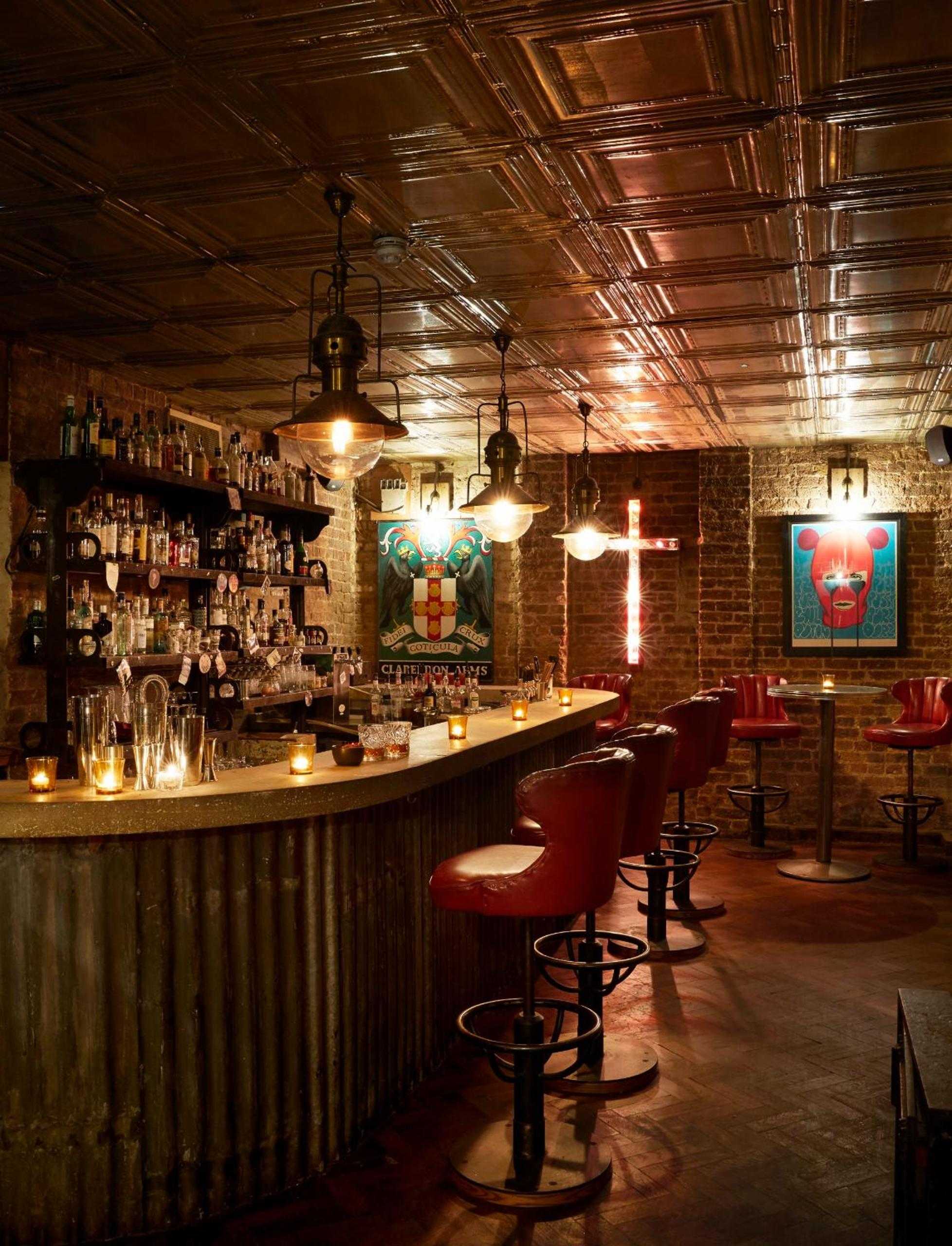 Exposed brick walls and burnished copper ceiling tiles create an intimate speakeasy atmosphere, where vintage pendant lights cast golden pools over leather bar stools and carefully curated cocktail collections.