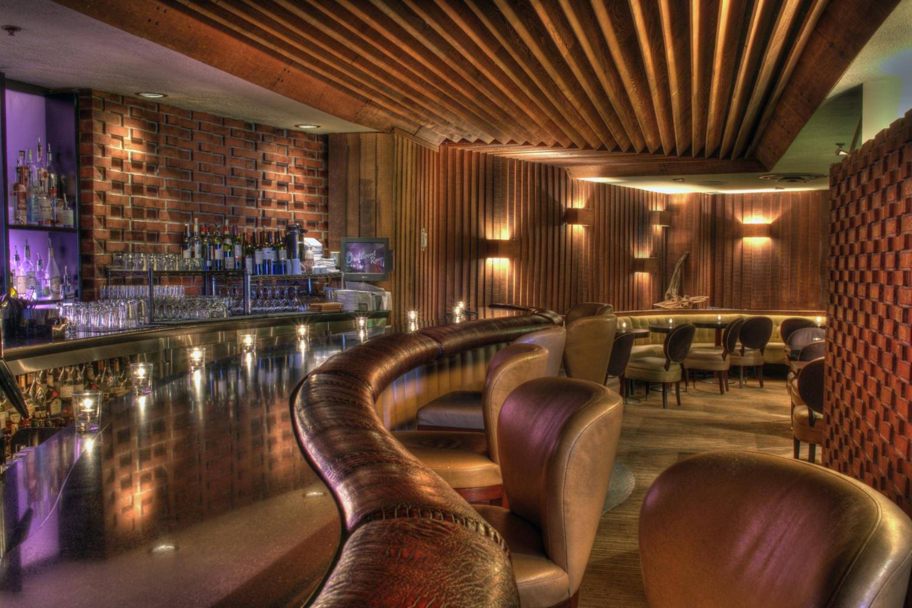Warm amber lighting dances across polished copper surfaces while leather banquettes curve invitingly around the intimate bar, where geometric brick walls meet sleek wood paneling.