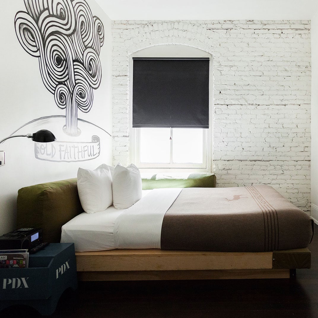 Minimalist design meets artistic flair in this thoughtfully curated guest room, where exposed white brick walls frame a striking black-and-white tree mural above the platform bed.