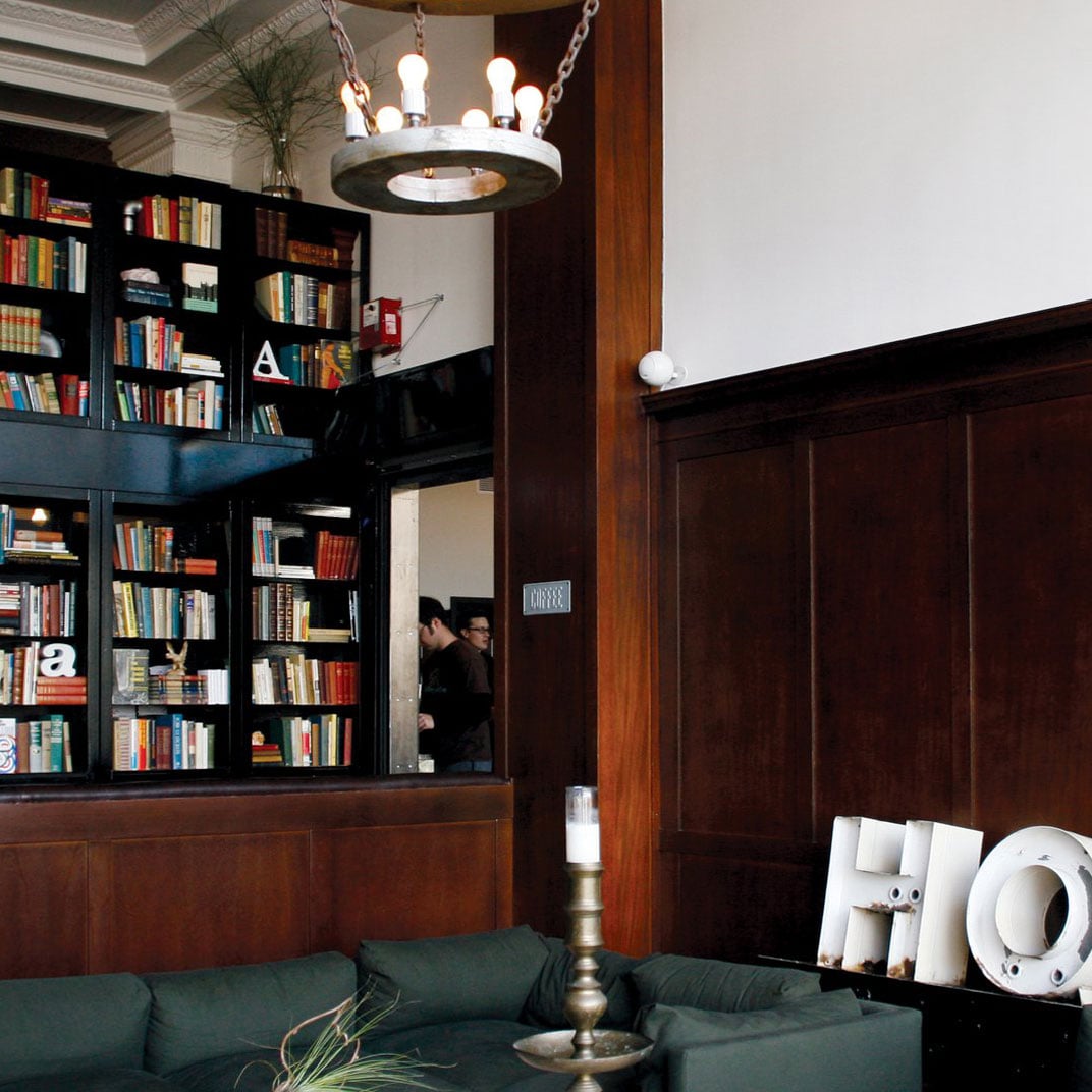 Rich walnut paneling and floor-to-ceiling bookshelves create an intimate library atmosphere in the sophisticated lobby lounge, anchored by emerald velvet seating and vintage brass accents.