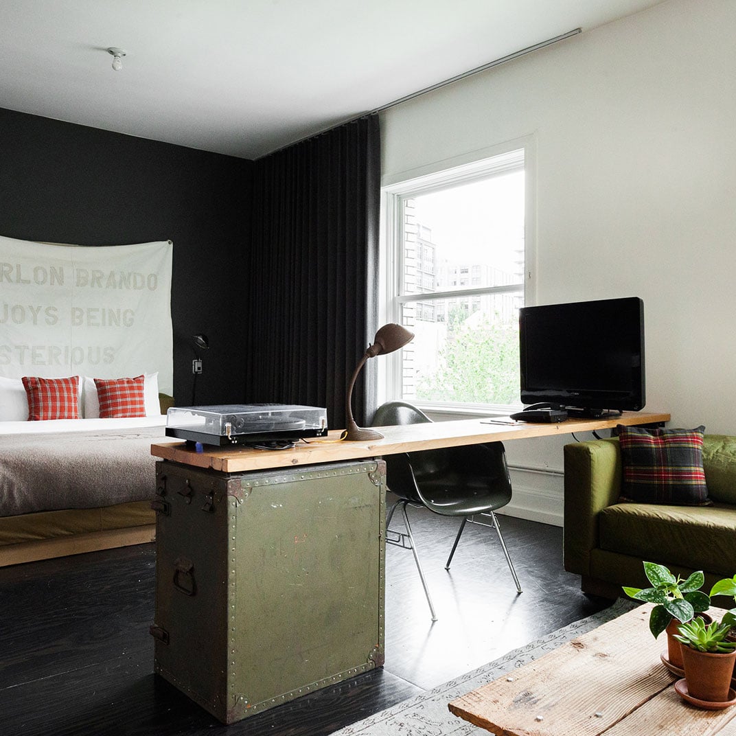 Industrial-chic meets cozy comfort with repurposed military trunks serving as desks, plaid accents adding warmth to dark wood floors and sleek modern furnishings.