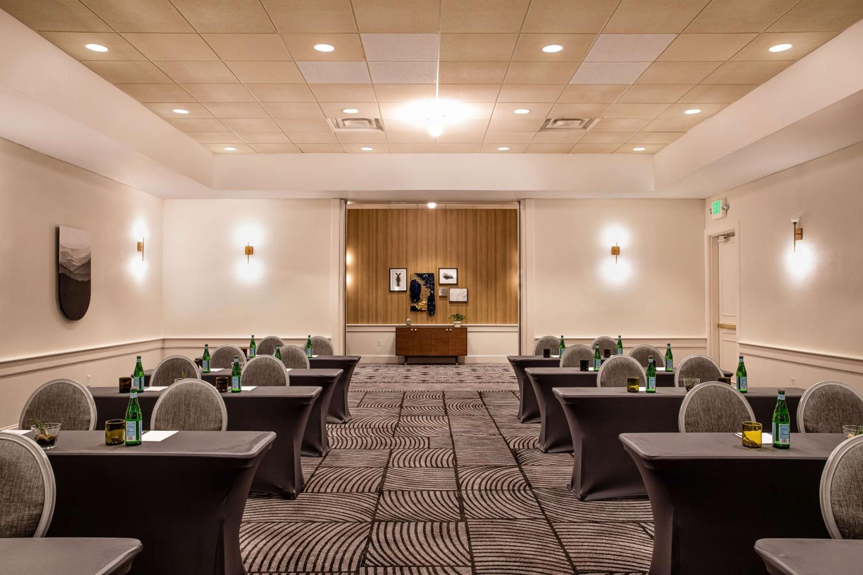 Warm wood paneling and contemporary geometric carpeting create an intimate boardroom atmosphere, where sparkling water awaits and natural light filters through sophisticated ceiling fixtures.