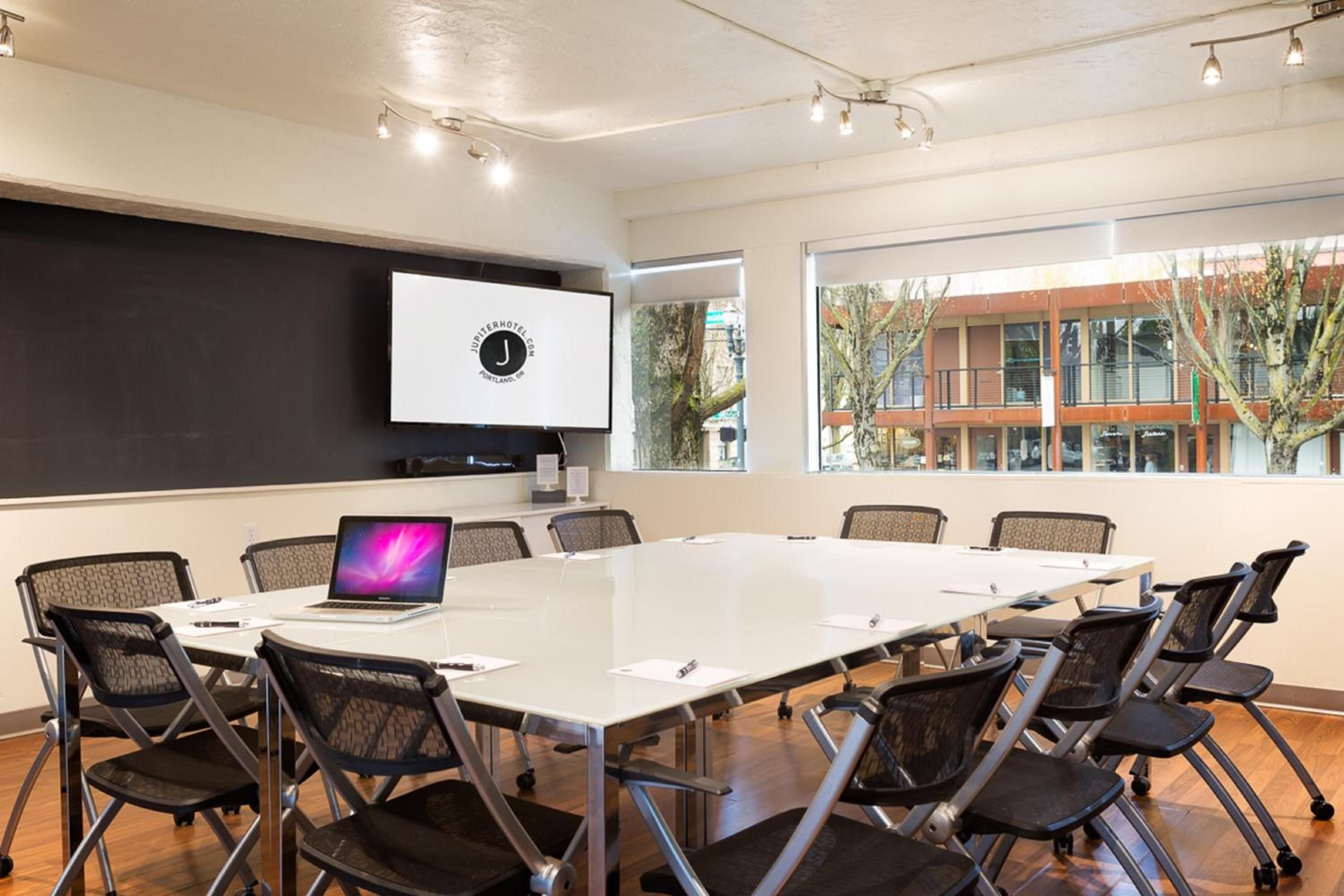 Natural light floods this sleek boardroom where modern mesh chairs surround polished tables, creating an inspiring workspace with street views of Portland's vibrant East Burnside corridor.