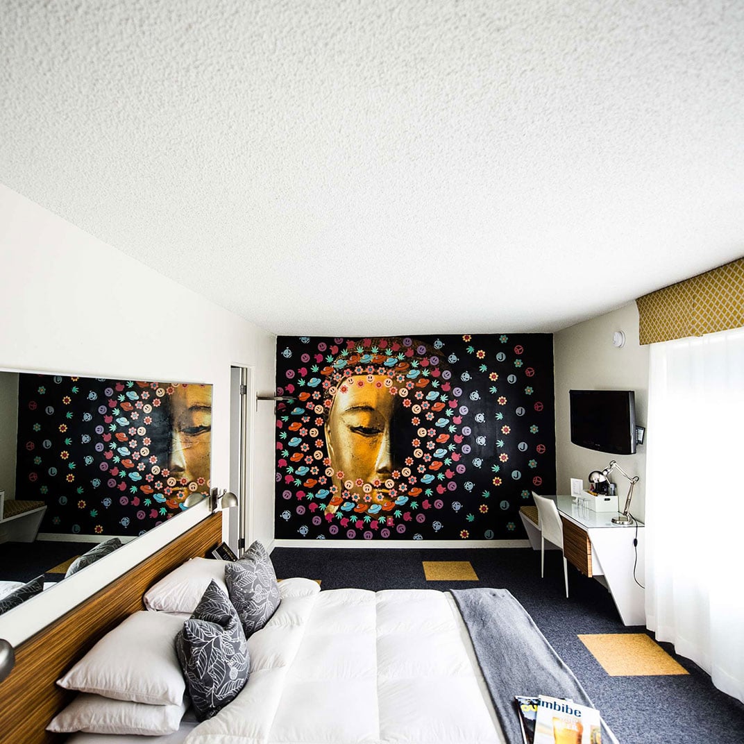 Golden Buddha artwork surrounded by vibrant floral motifs creates an unexpected zen focal point against crisp white linens and rich wood accents in this thoughtfully curated space.