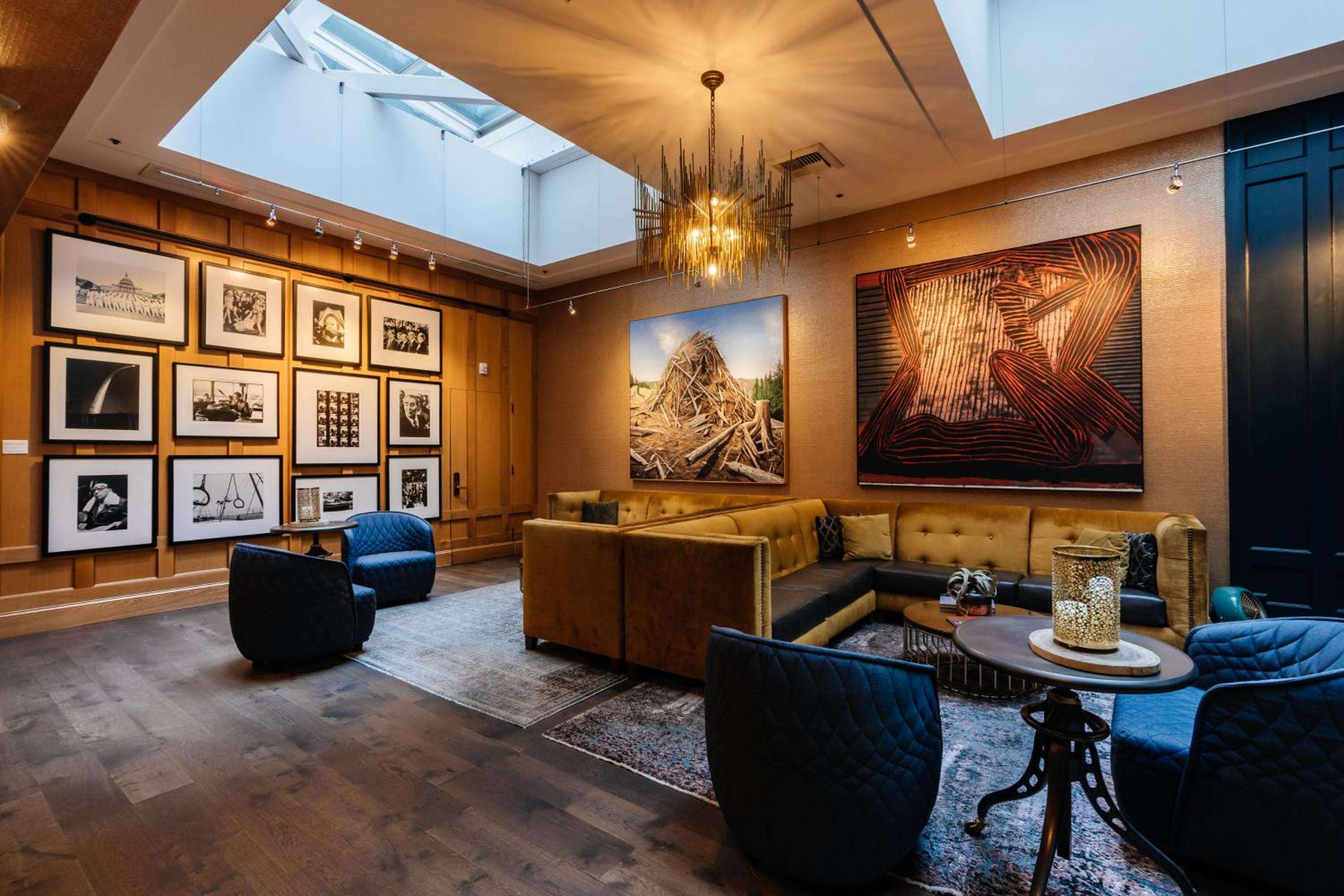Warm wood paneling and curated photography create an intimate gallery-like lounge, where golden light filters through skylights onto plush velvet seating and rich leather banquettes.