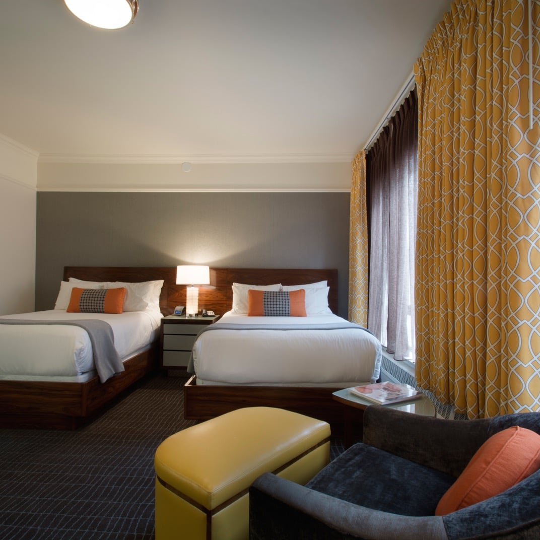 Twin beds anchor this thoughtfully appointed suite where golden geometric wallpaper creates visual warmth against charcoal accents and rich wood headboards.