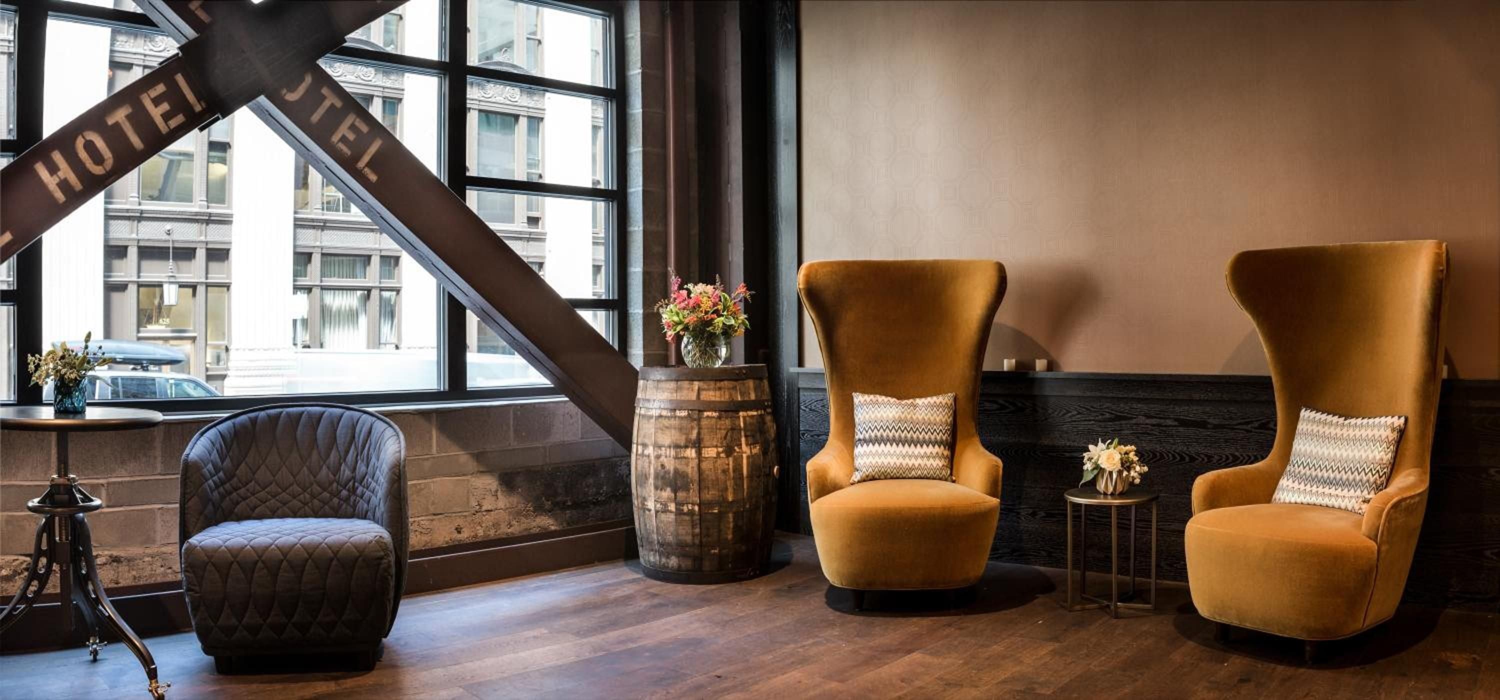 Mustard velvet wingback chairs and weathered whiskey barrels create an inviting respite beneath exposed steel beams, where industrial heritage meets contemporary comfort.