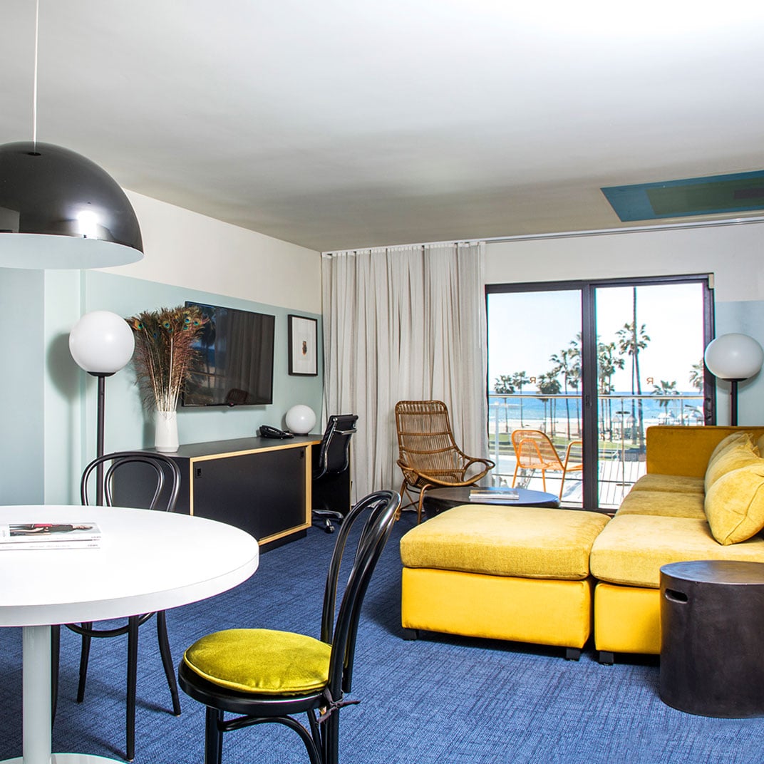 Sunny yellow sectionals and navy carpeting create a vibrant coastal vibe in this suite, where floor-to-ceiling windows frame Venice Beach's palm-studded horizon.