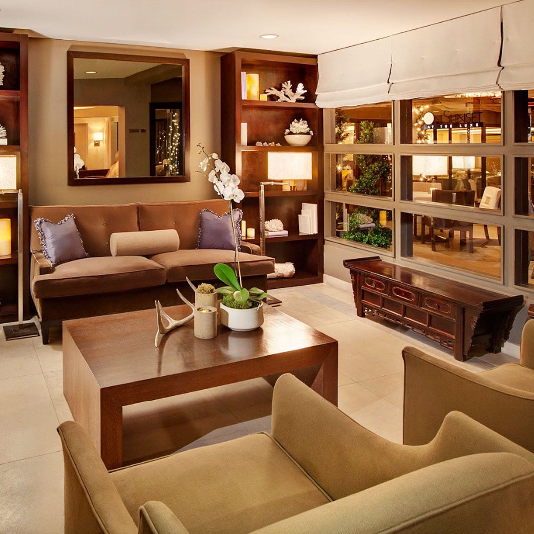 Warm wood tones and neutral furnishings create an inviting retreat in the lobby, where built-in shelving displays curated objects and orchids add delicate touches.
