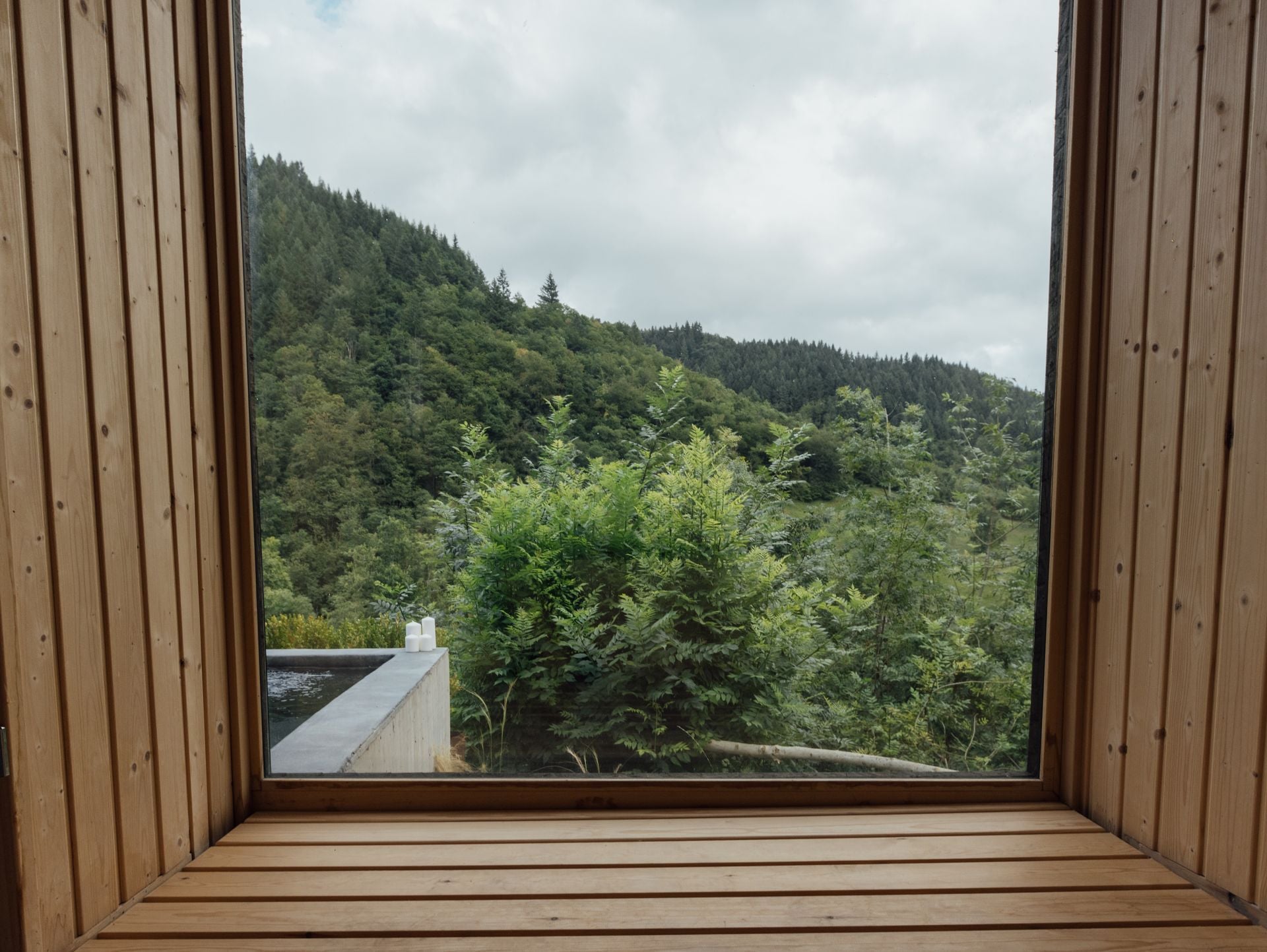 Natural wood frames capture rolling forested hills from this thoughtfully designed window seat, where warm timber textures complement the lush Welsh valley beyond.
