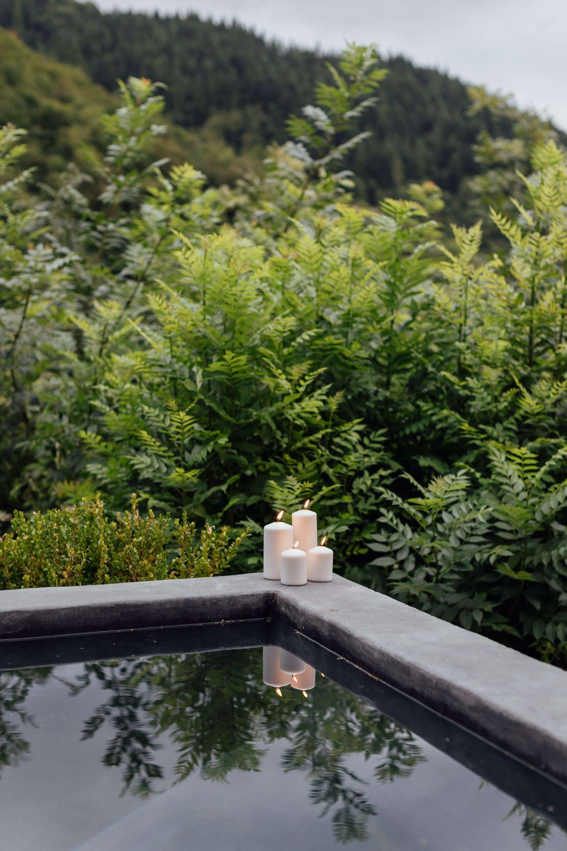 Flickering candles cast gentle reflections across still waters while ancient ferns whisper in the highland breeze, creating an intimate sanctuary for evening contemplation.