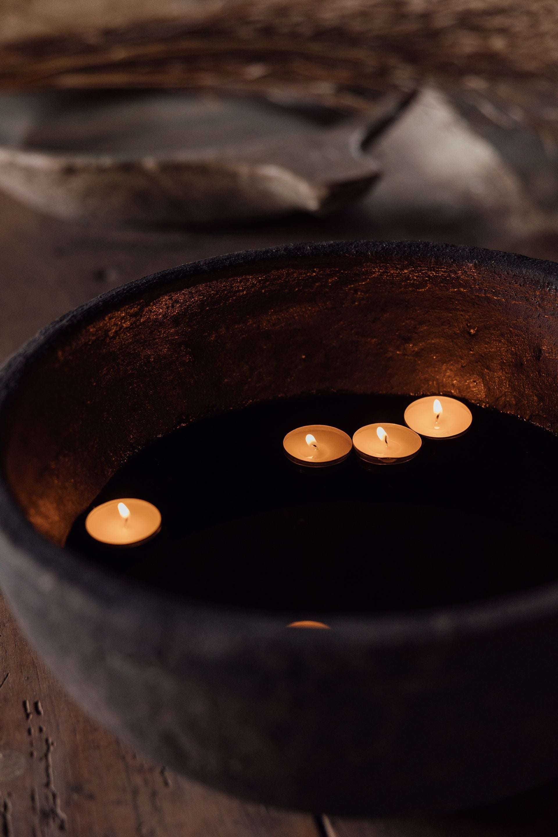Floating tea lights cast amber reflections across dark water in a rustic stone basin, creating an intimate sanctuary where ancient wellness traditions meet modern luxury.