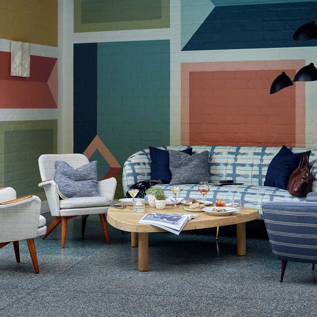 Bold geometric murals create an artistic backdrop for intimate conversations over wine in this mid-century modern lounge, where navy textiles meet warm wood tones.