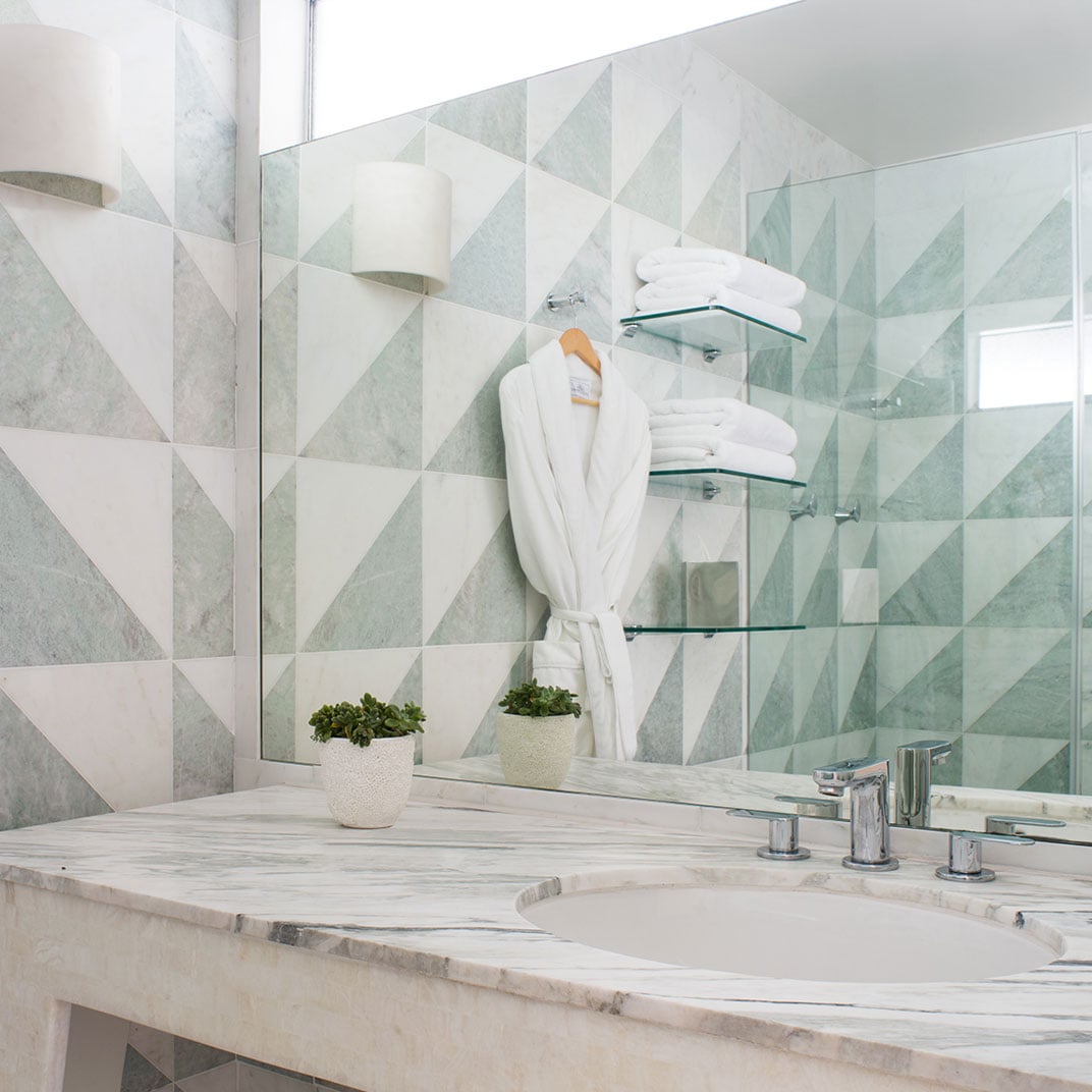 Geometric mint and white tiles create a striking backdrop for marble vanities, where plush robes and glass shelves add spa-like luxury to every morning ritual.