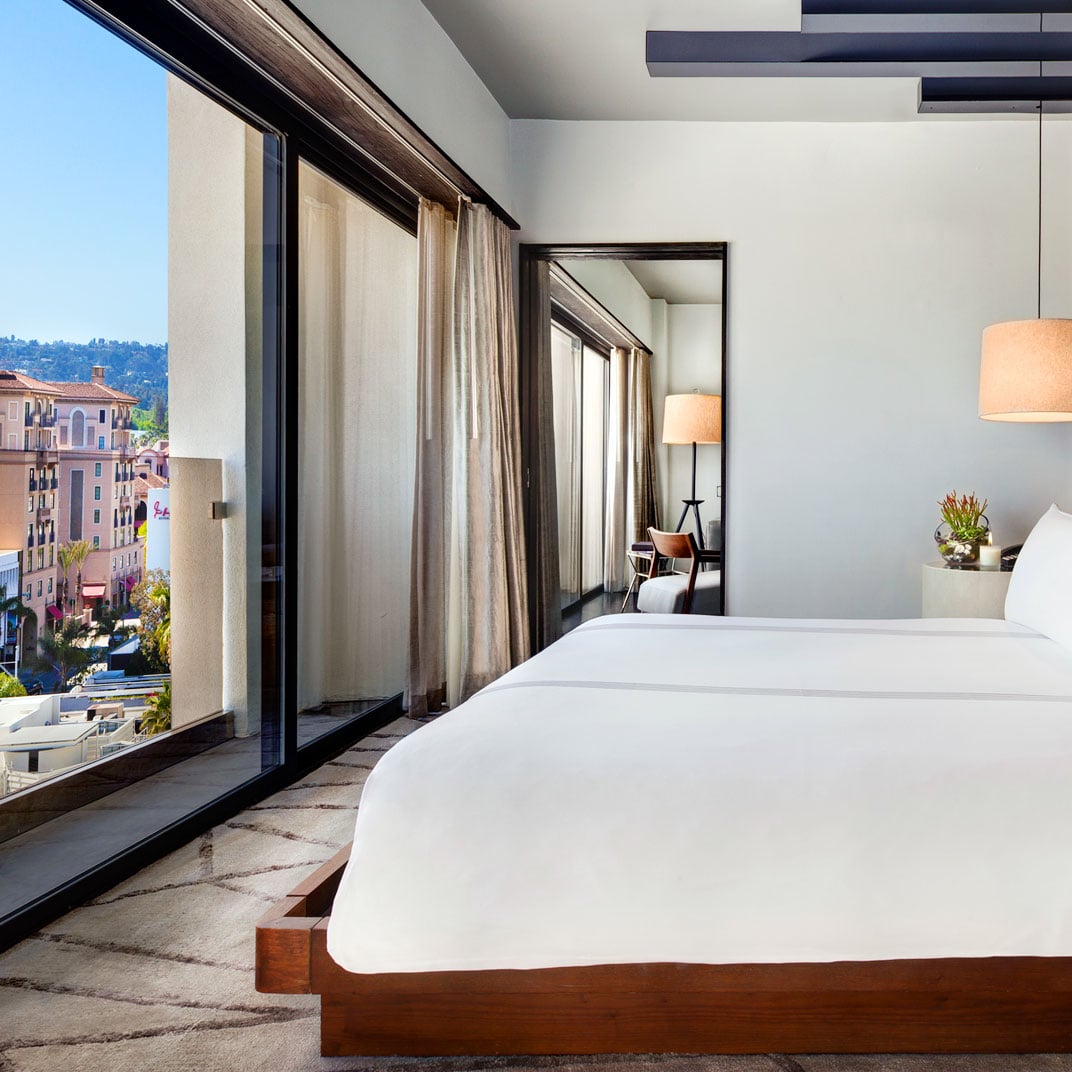 Floor-to-ceiling windows frame Beverly Hills rooftops from this sleek suite, where warm wood tones and crisp linens create an understated sanctuary above the city.