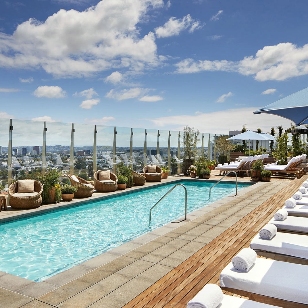 Crystal-clear waters reflect wispy clouds while wicker loungers and wooden decking frame sweeping city vistas from this serene rooftop sanctuary.