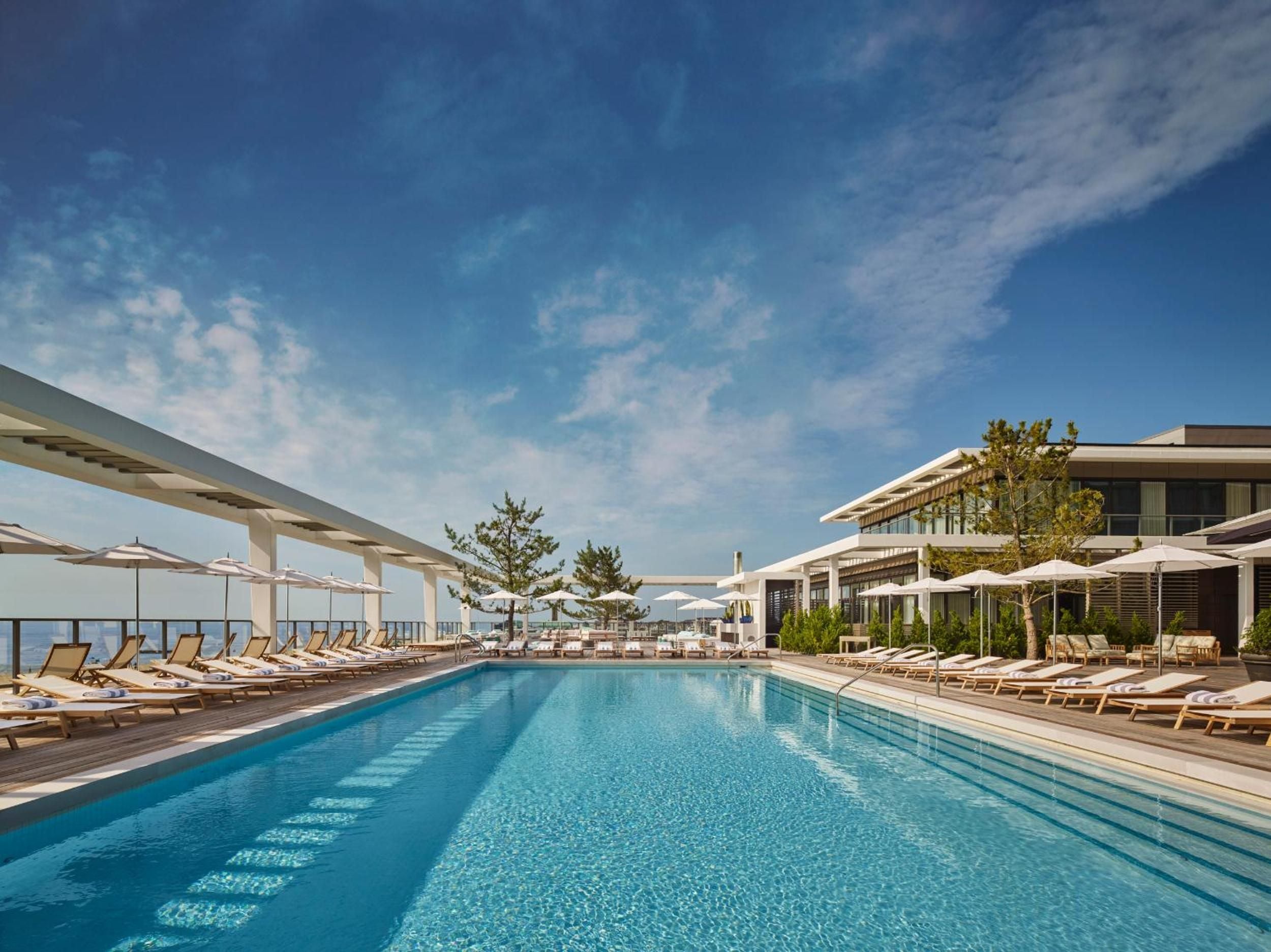 Sun-drenched loungers frame the crystalline pool where modern architecture meets coastal serenity, creating an sophisticated oceanfront sanctuary beneath endless blue skies.