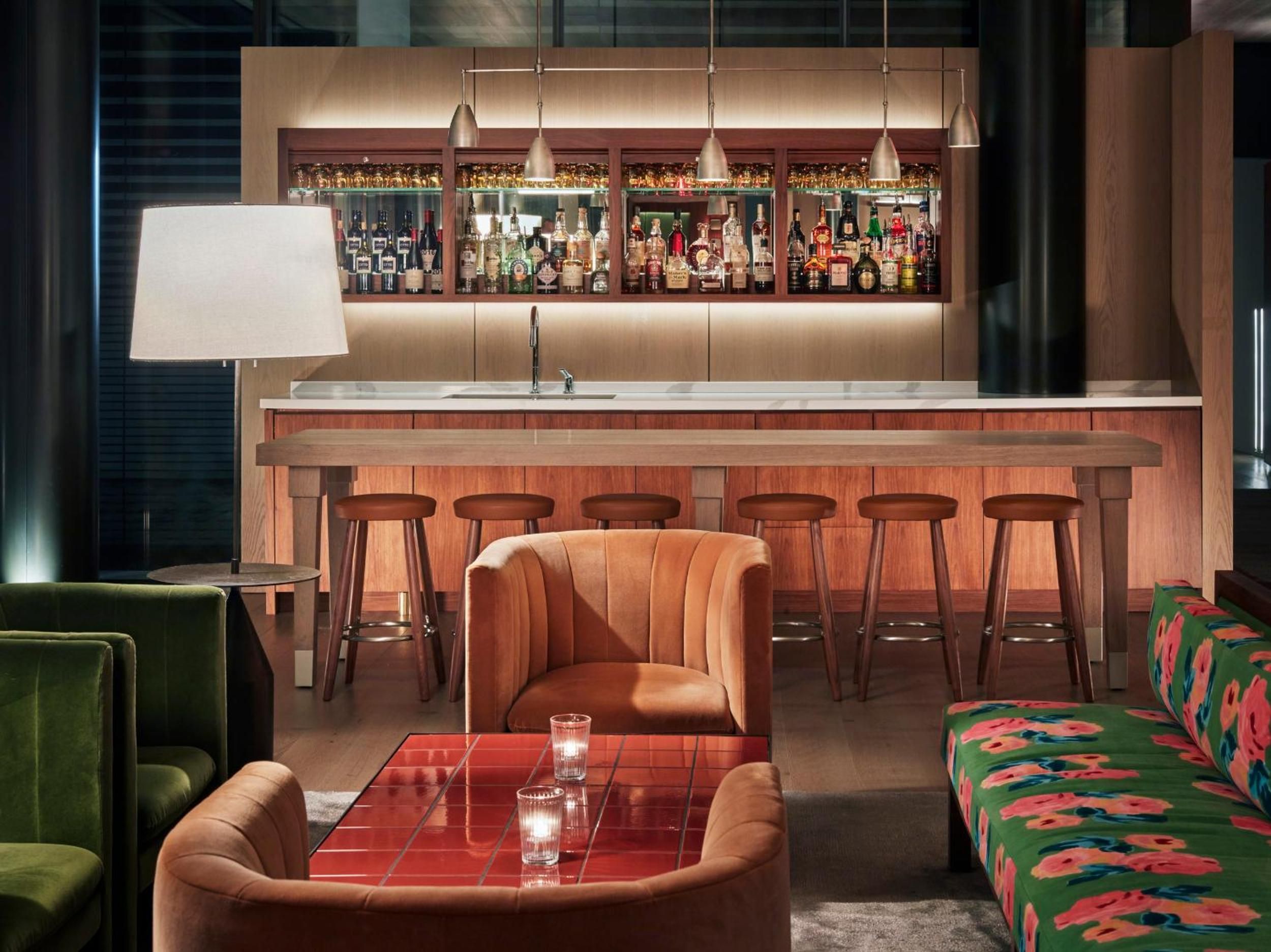 Warm walnut millwork and jewel-toned velvet seating create an intimate cocktail haven, where pendant lights cast a golden glow over the expertly curated spirits collection.