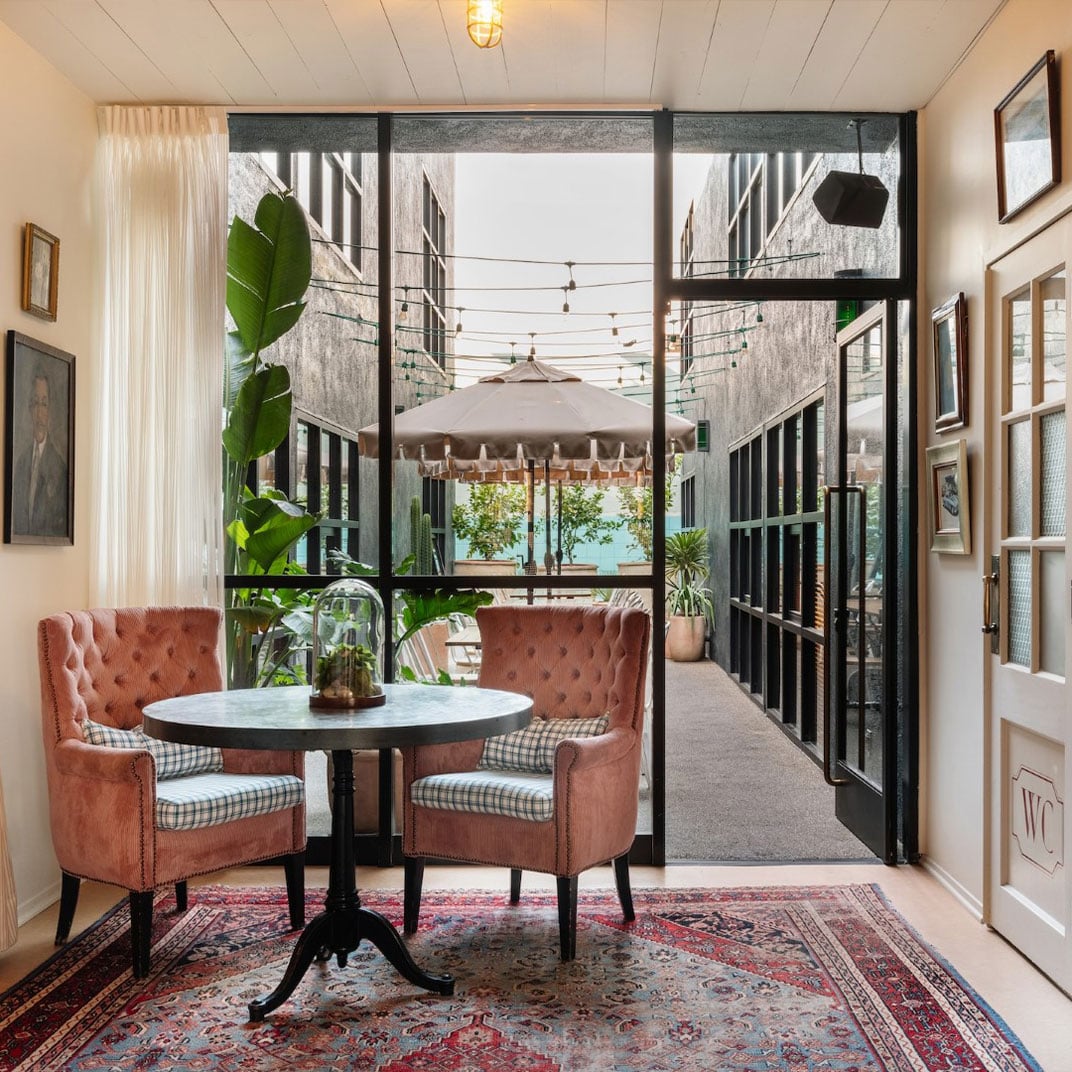 Burnt orange velvet chairs and Persian rugs create an intimate nook where string lights dance beyond floor-to-ceiling windows, blending cozy sophistication with courtyard charm.