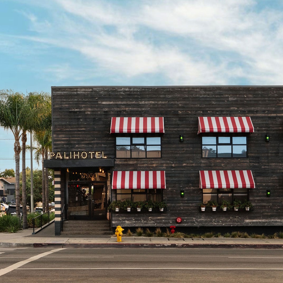 Charcoal wood siding and candy-striped awnings give this West Hollywood boutique hotel a playful main-street charm beneath swaying palms and endless California sky.