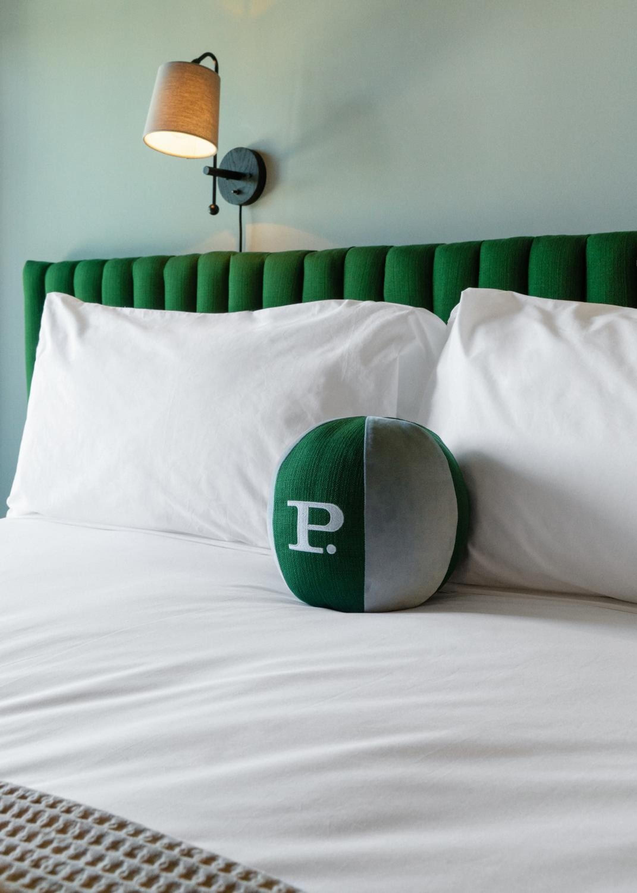 Emerald velvet headboards and custom monogrammed pillows create intimate sleeping quarters where mid-century charm meets contemporary comfort in perfectly curated guest rooms.