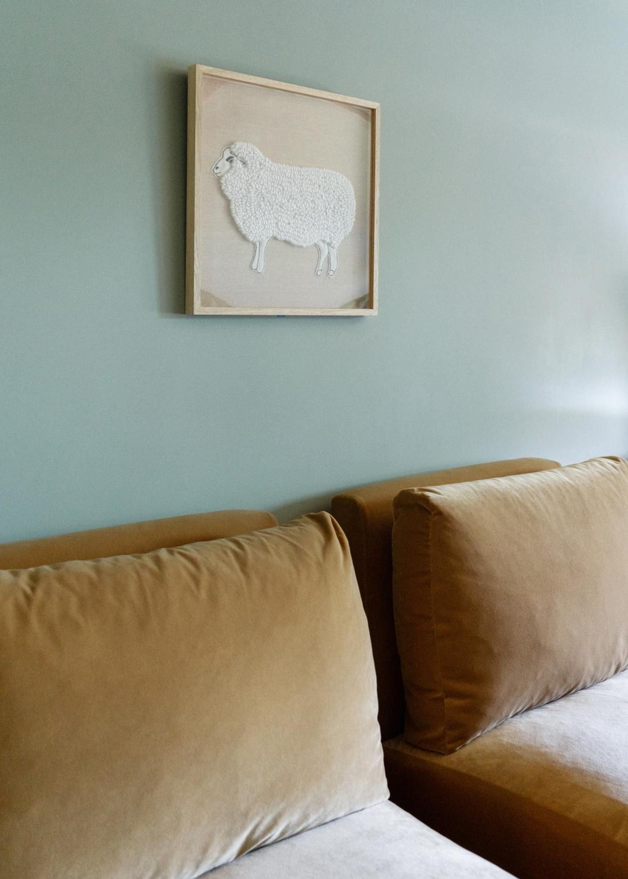 Soft sage walls frame whimsical sheep artwork above plush camel-toned cushions, creating an unexpectedly playful yet sophisticated corner that perfectly captures the hotel's creative spirit.