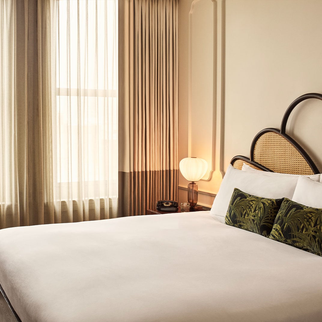 Warm afternoon light filters through layered curtains, illuminating the cane headboard and tropical-print pillows that give this downtown retreat its signature bohemian sophistication.