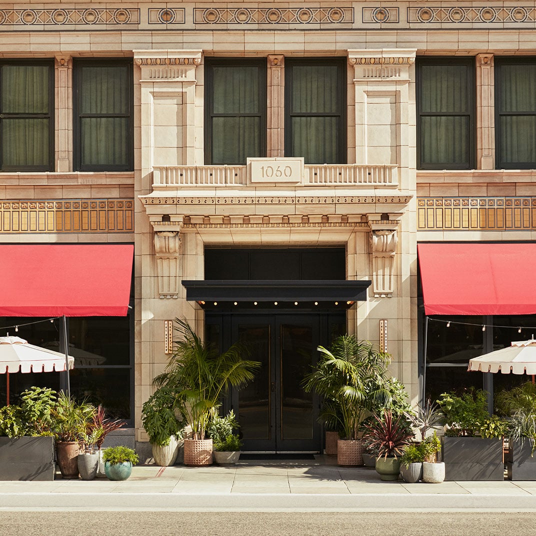 Art Deco grandeur meets modern hospitality as ornate stonework and geometric patterns frame the hotel's inviting entrance, where coral awnings and tropical plantings soften the building's historic formality.