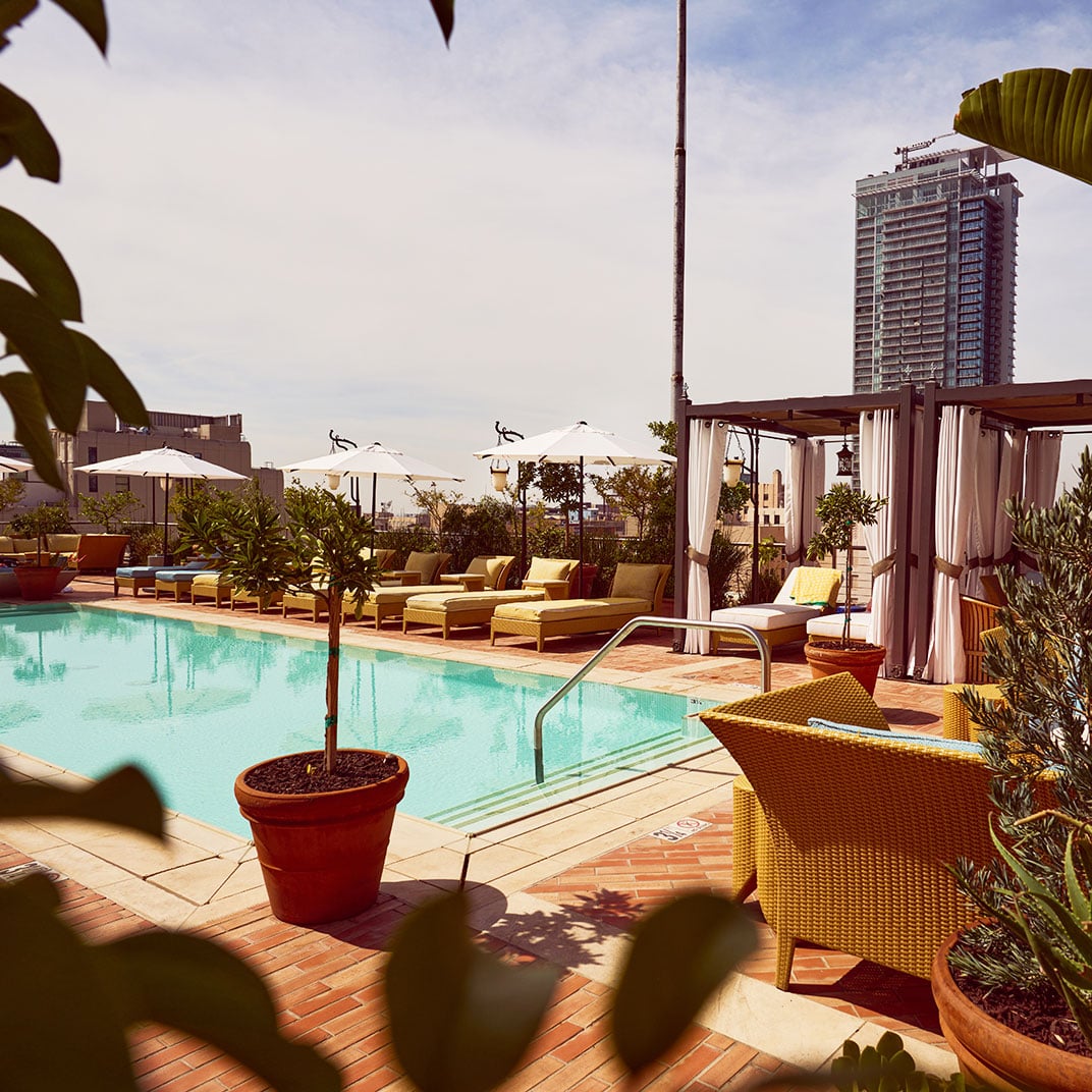 Golden hour bathes the rooftop pool deck in warm light, where cabanas and loungers create intimate retreats against the downtown skyline backdrop.