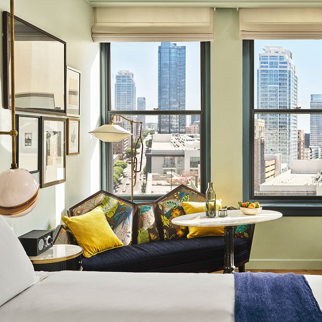 Corner windows frame Seattle's skyline from this sophisticated suite, where tropical-print pillows and brass accents create an intimate reading nook bathed in golden afternoon light.