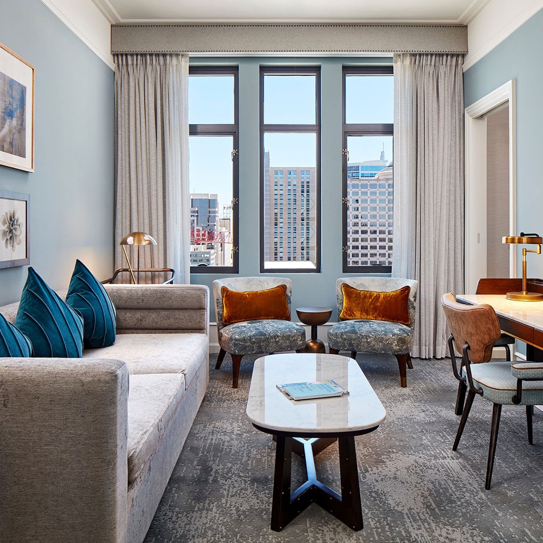 Velvet armchairs in burnished copper face floor-to-ceiling windows overlooking the city, while teal accent pillows add unexpected warmth to this sophisticated suite.