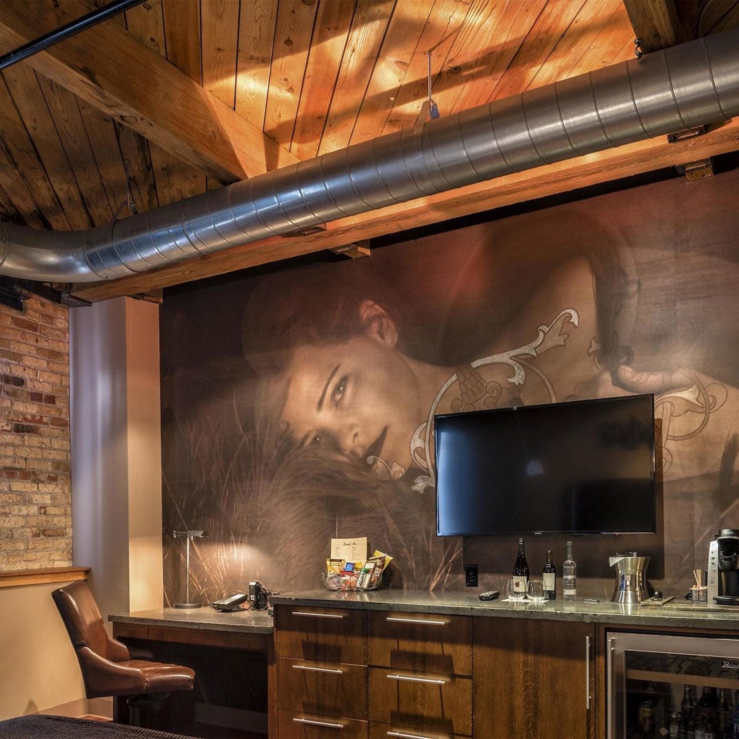 Exposed brick meets industrial ductwork in this intimate bar nook, where a striking portrait mural creates dramatic backdrop for craft cocktails and bourbon tastings.