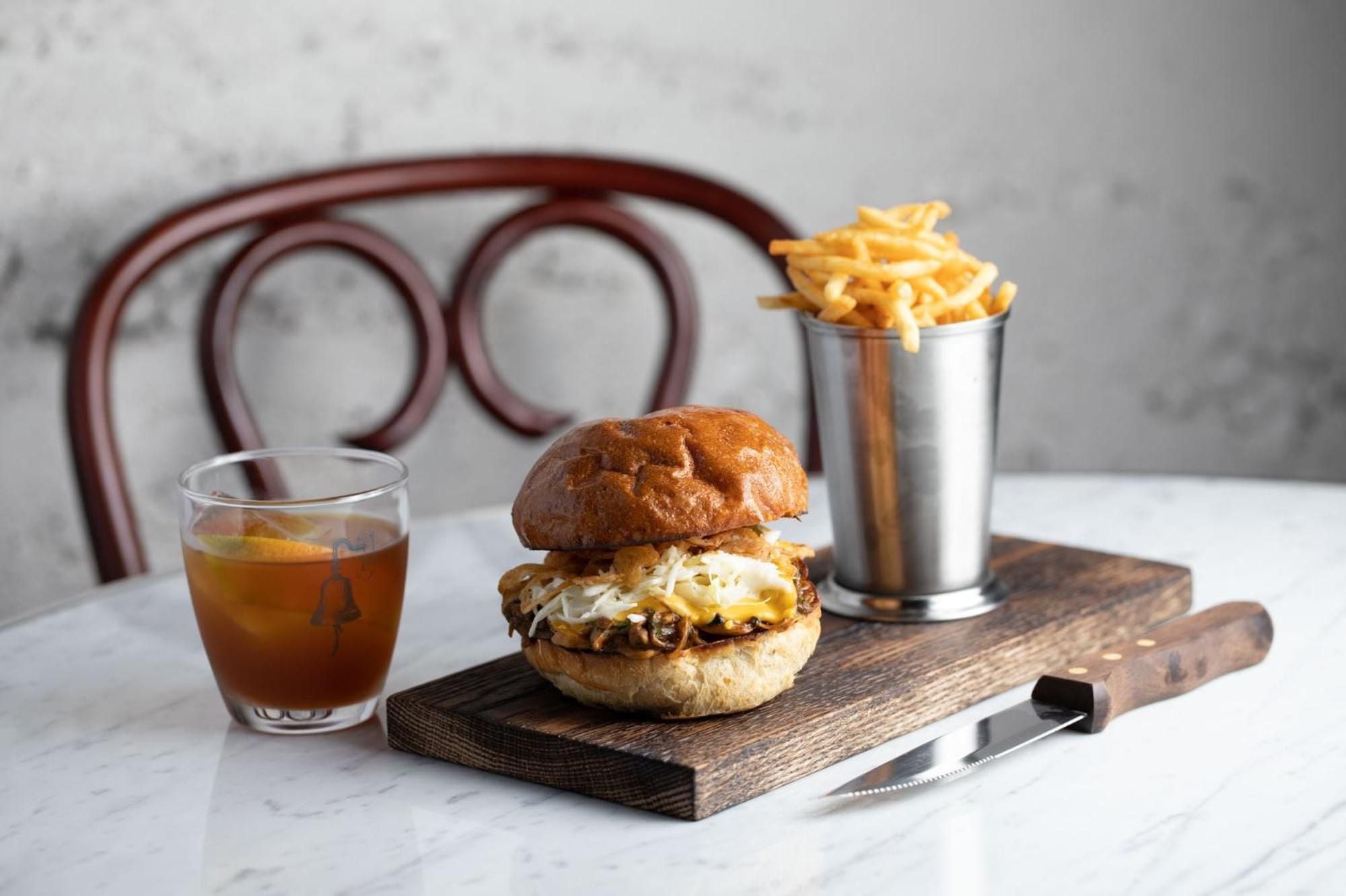Gourmet comfort meets artisanal craft on weathered wood, where golden fries cascade from metal cups alongside perfectly stacked burgers and amber-hued cocktails.