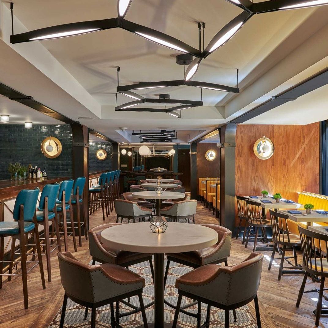 Geometric pendant lights cast warm pools of light over curved banquettes and rich wood paneling, creating an intimate yet energetic dining atmosphere perfect for lingering conversations.