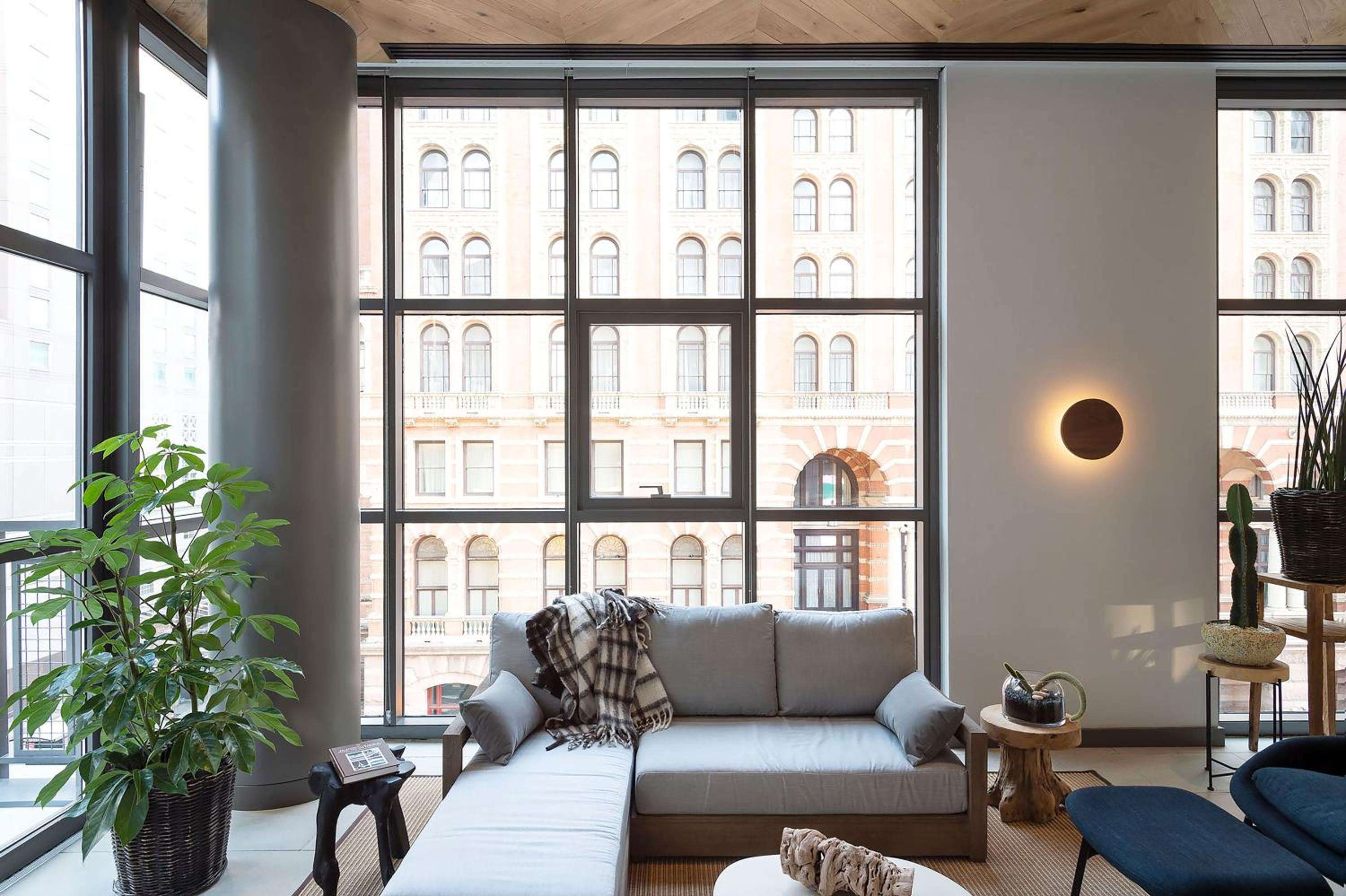 Floor-to-ceiling windows frame historic Philadelphia architecture while warm wood ceilings and minimalist furnishings create an urban sanctuary above the bustling streets below.