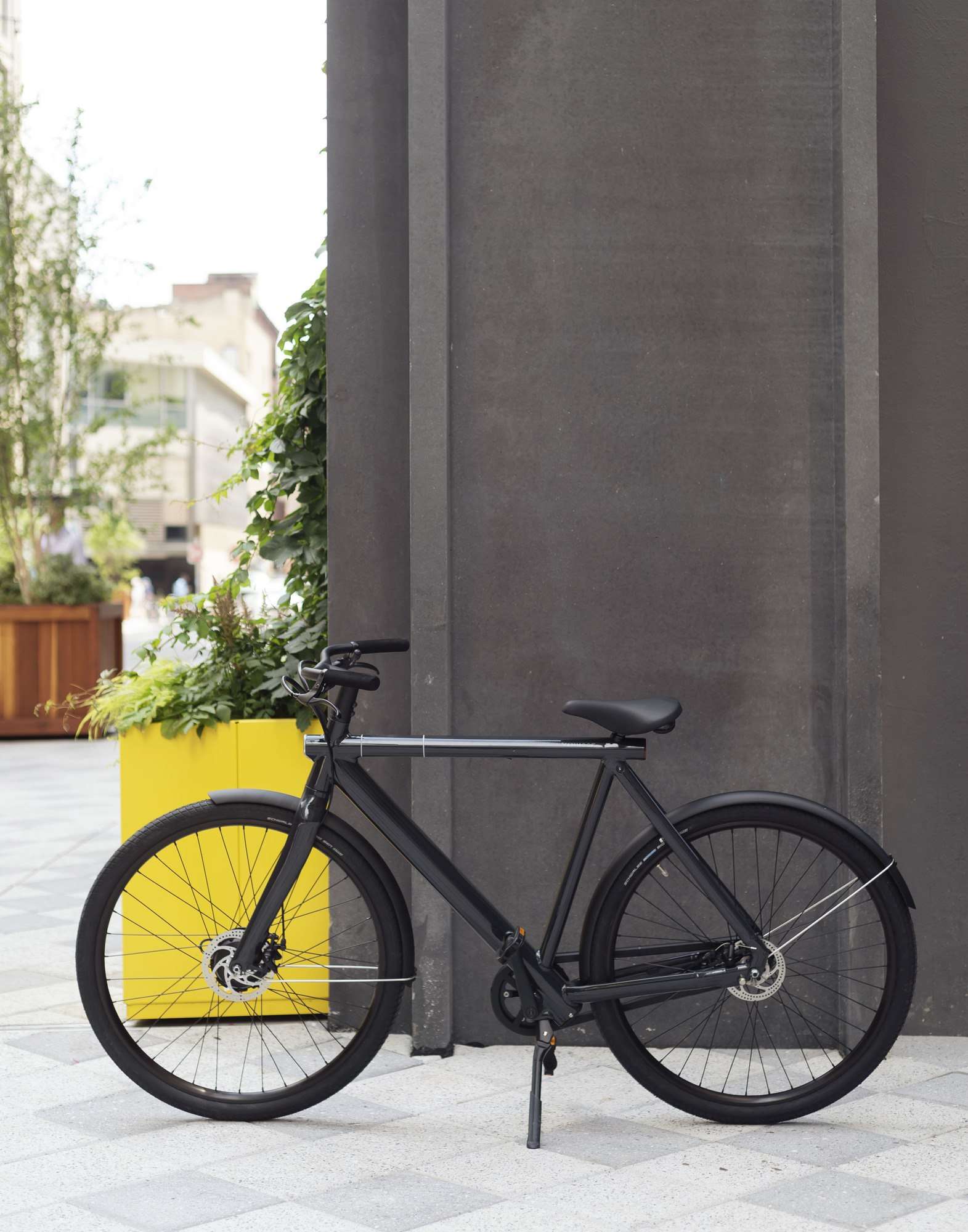 Sleek black bicycles lean against concrete pillars, ready for urban exploration beyond bright yellow planters that punctuate the modern courtyard's minimalist aesthetic.