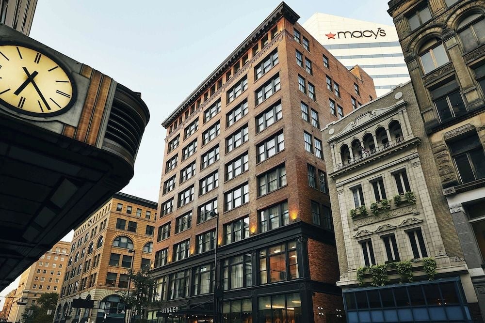 Historic brick facades and ornate stonework frame the hotel's urban setting, where a vintage street clock marks time against Cincinnati's architectural tapestry.
