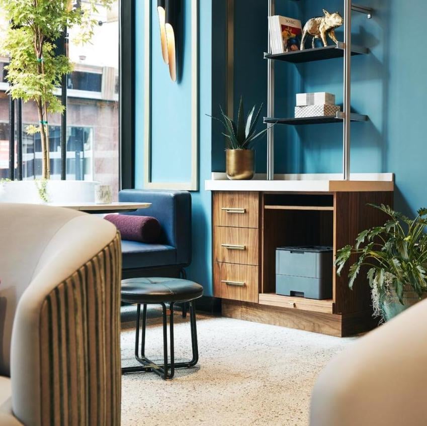 Warm walnut furnishings and jewel-toned blue walls create an intimate reading nook, where afternoon light filters through oversized windows onto plush seating and thoughtful design details.