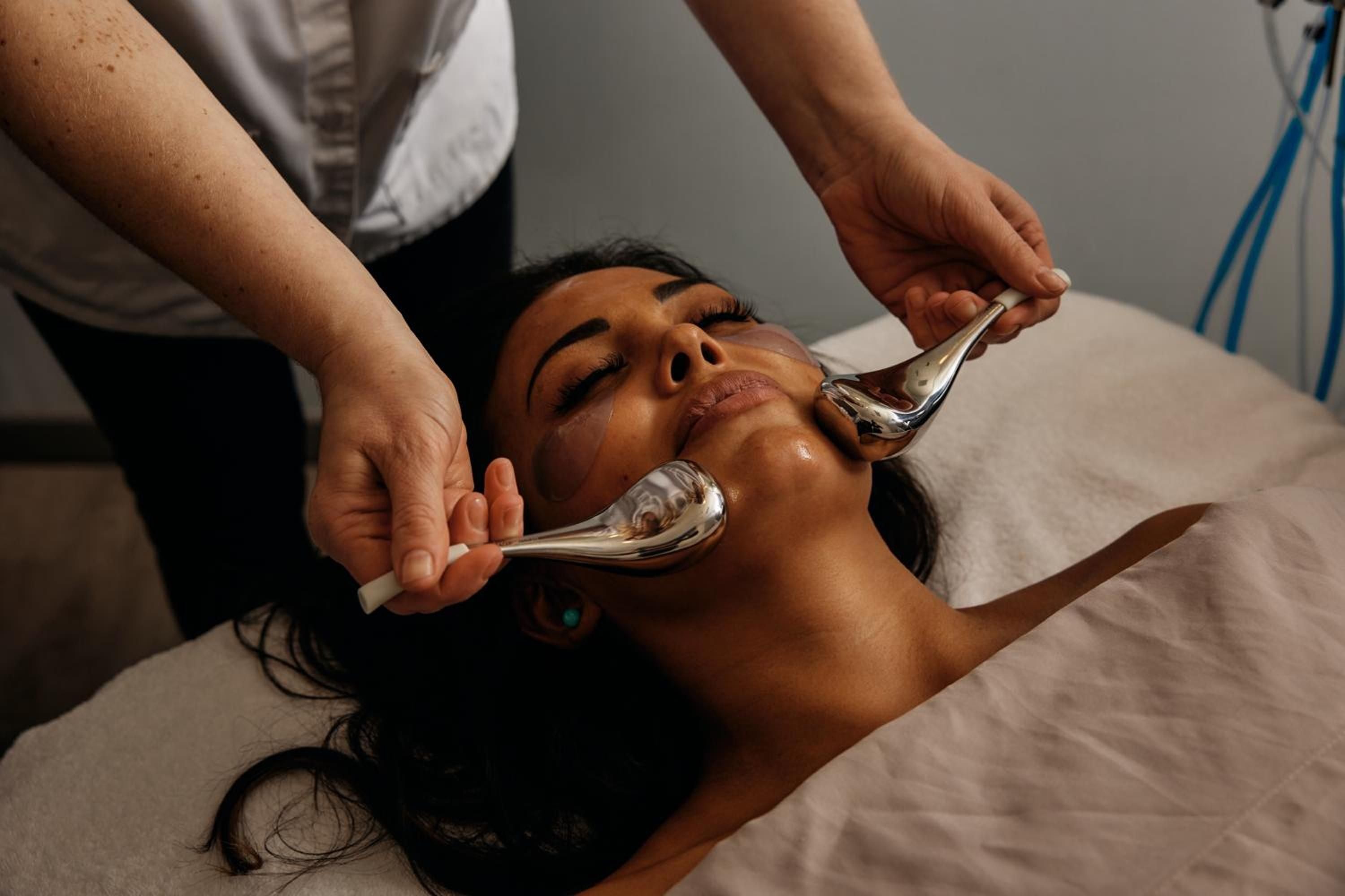 Skilled hands guide chrome facial tools across skin in Still Spa's serene treatment rooms, where Lake Washington's tranquil energy infuses every therapeutic touch.