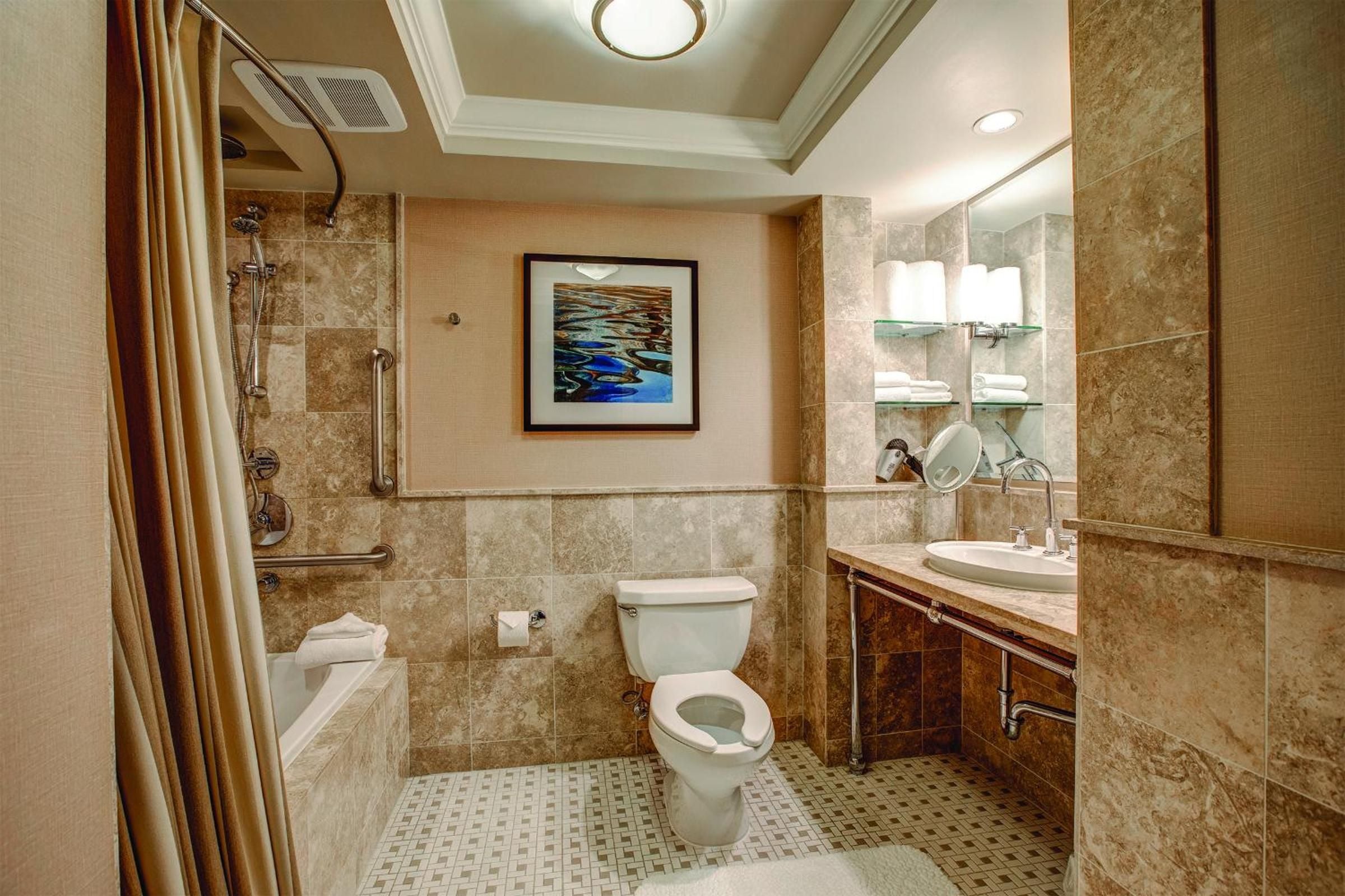 Warm travertine tiles and rich wood vanities create a spa-like sanctuary, while accessible features ensure comfort without compromising the sophisticated lakeside aesthetic.