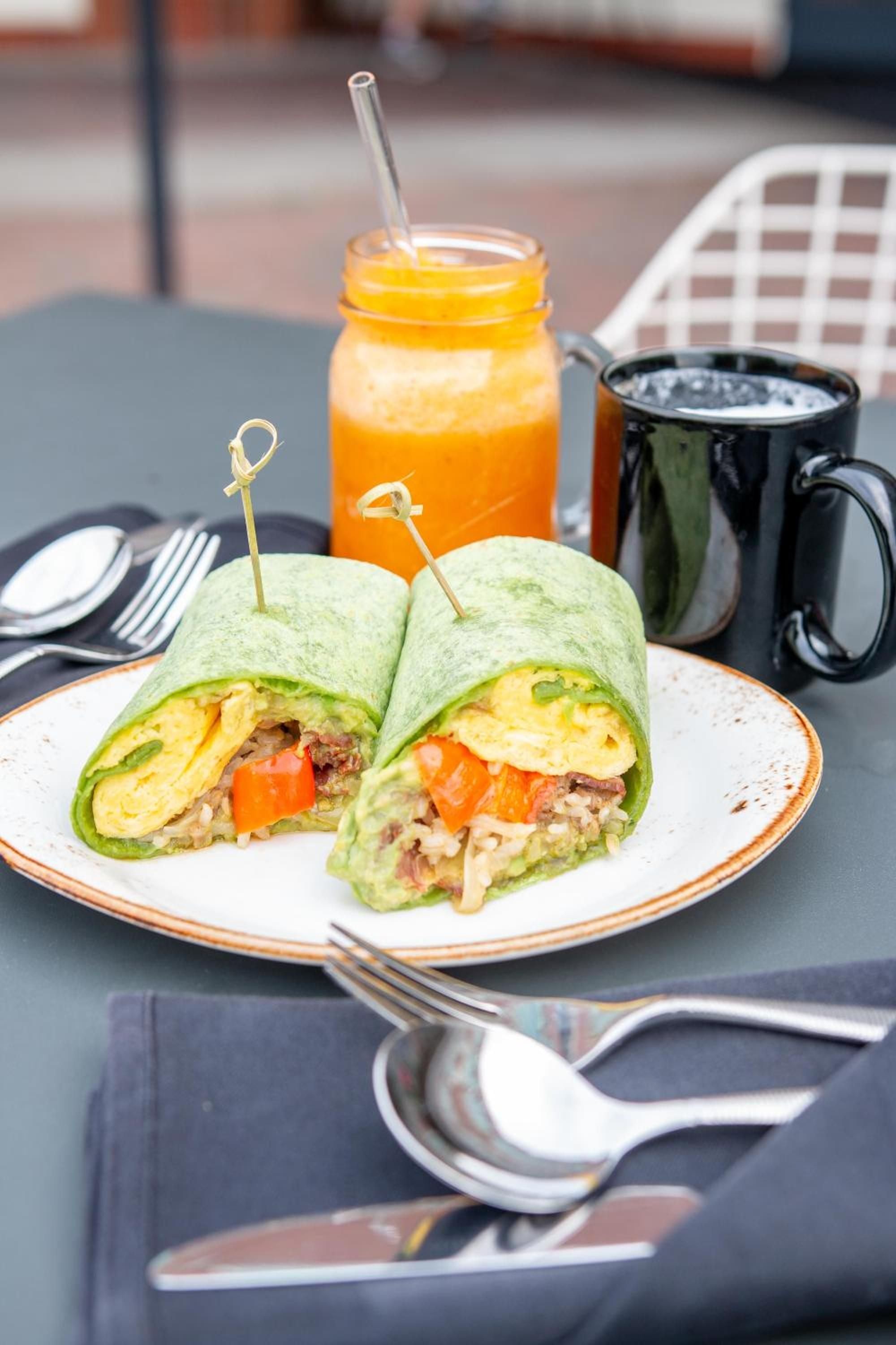 Fresh breakfast wraps burst with scrambled eggs and vibrant vegetables, paired with golden juice and steaming coffee on the lakeside terrace.