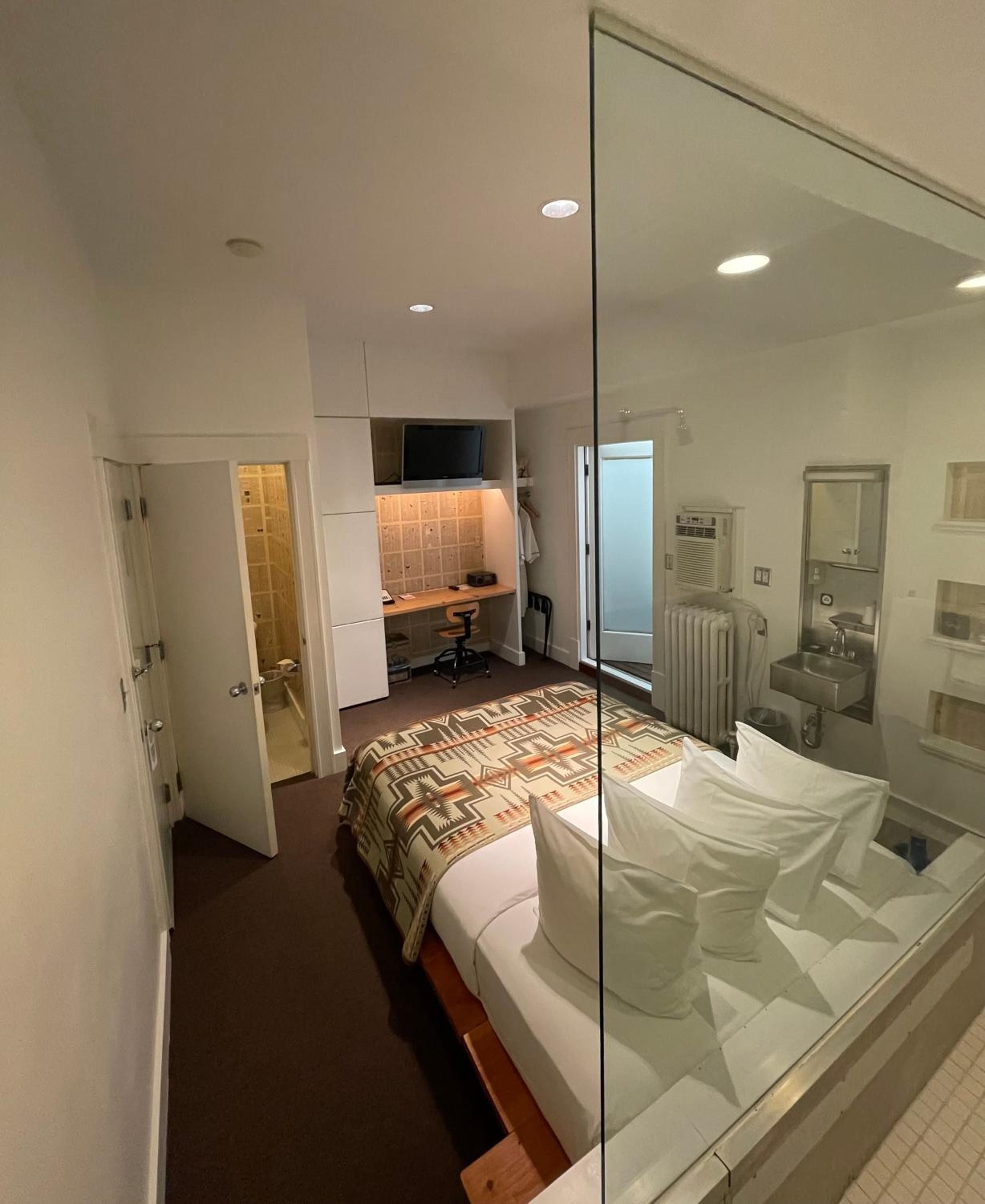 Glass walls dissolve boundaries between sleeping and bathing spaces, while geometric throws and warm wood accents soften the minimalist urban aesthetic.
