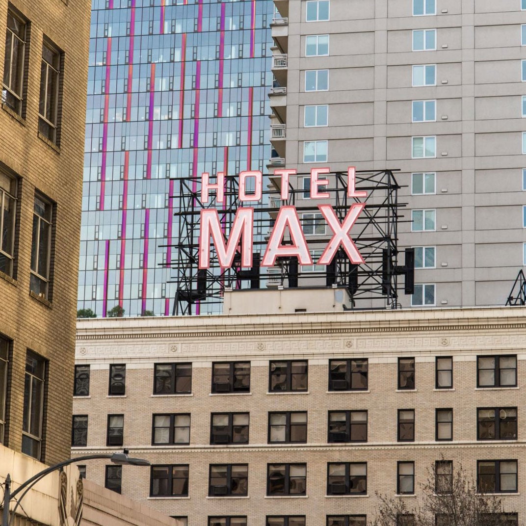 Bold pink neon lettering crowns this converted 1920s building, where historic brick meets modern glass towers in Seattle's bustling downtown theater district.