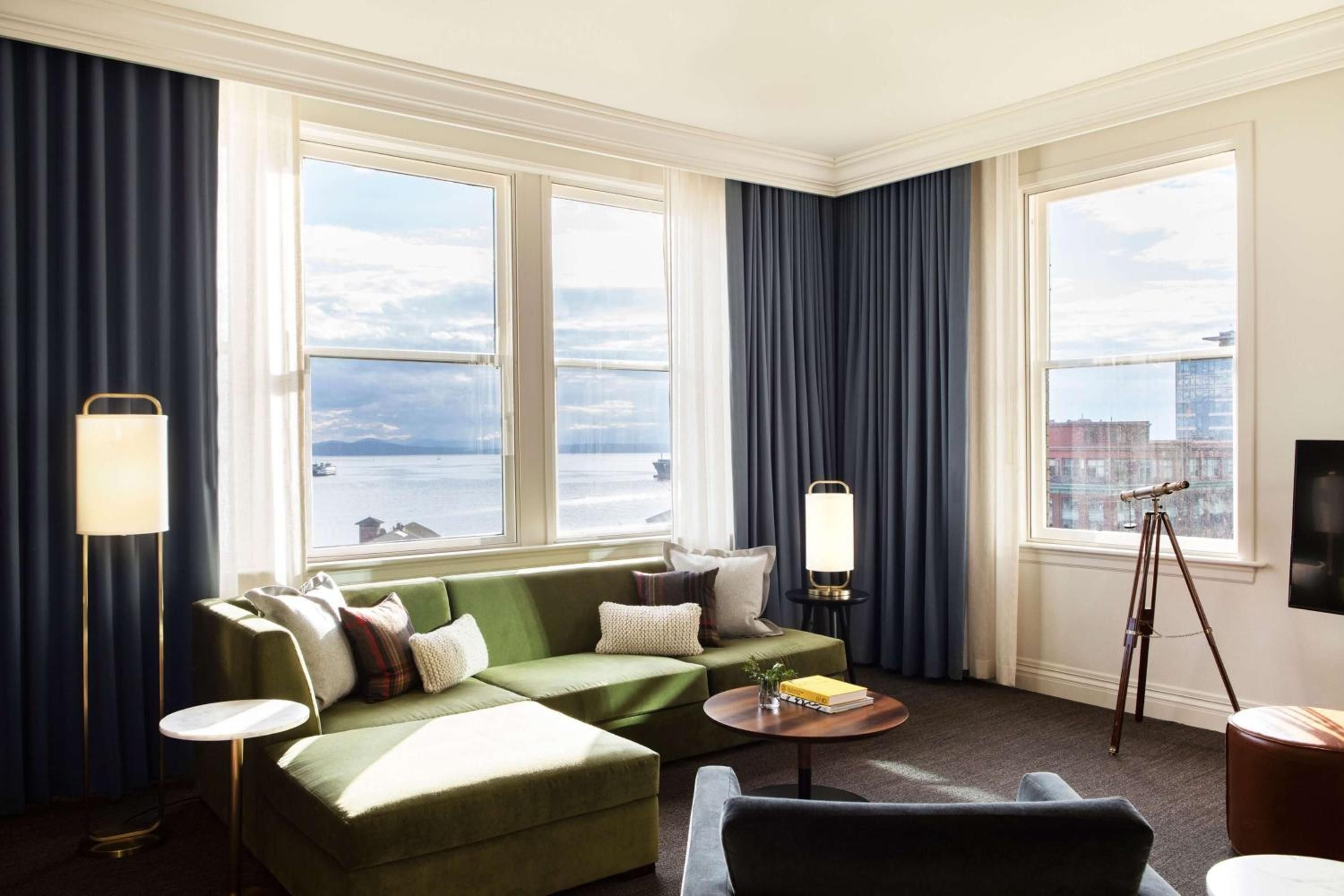 Corner windows frame Elliott Bay's shimmering waters while sage velvet furnishings and brass accents create an inviting retreat high above Seattle's bustling waterfront.