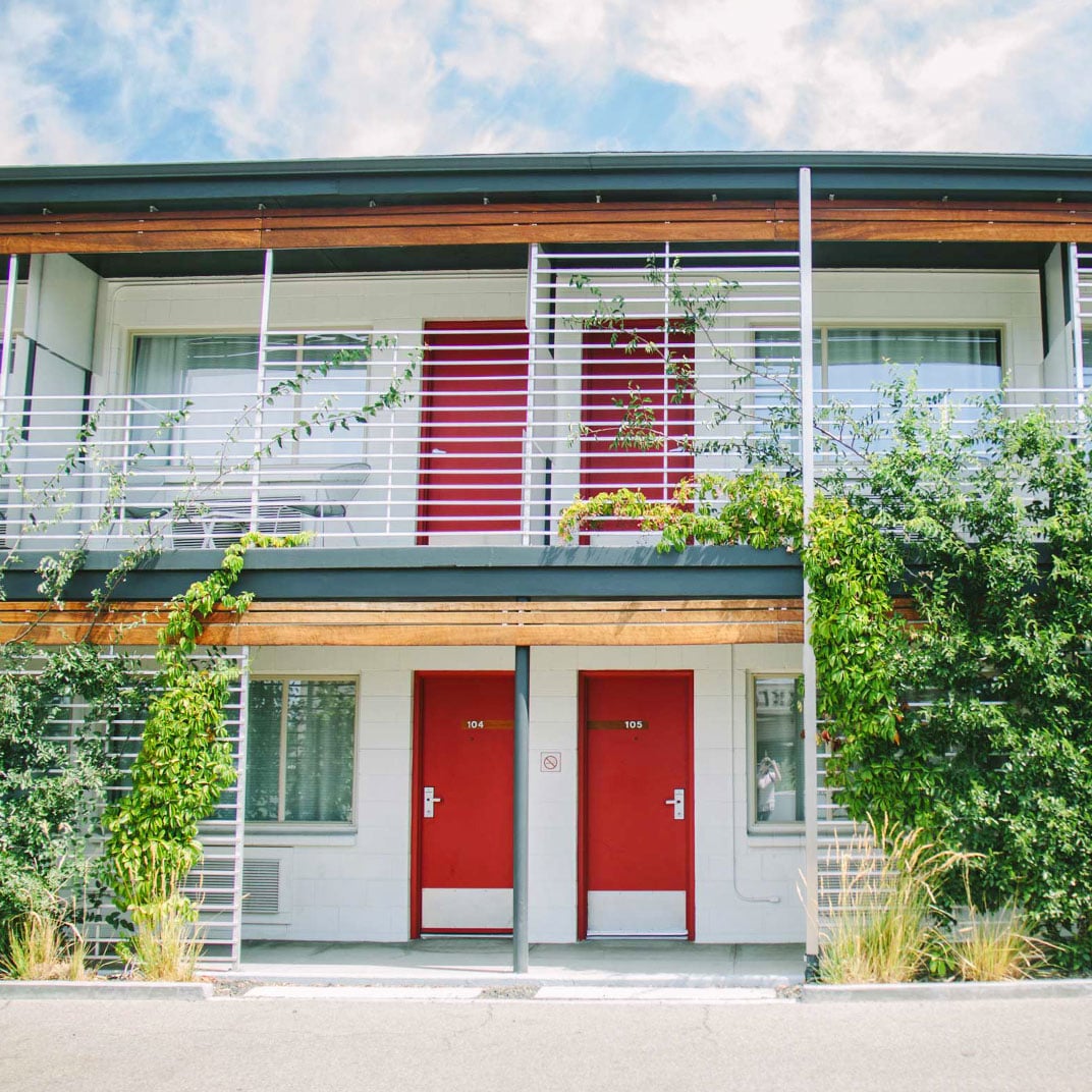 Striking red doors punctuate the modern facade, while climbing vines soften geometric lines and horizontal wood accents add warmth to this contemporary retreat.