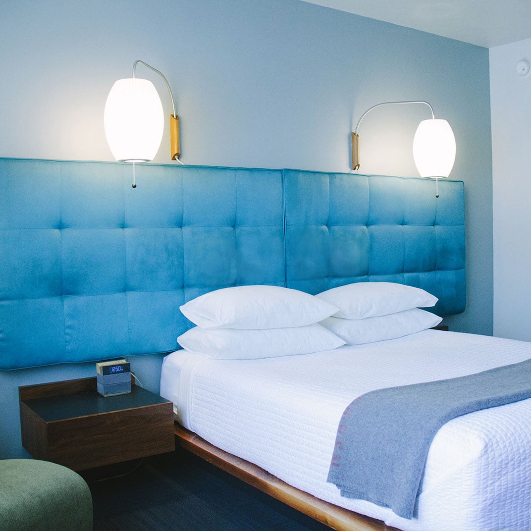 Tufted blue headboards and sculptural pendant lamps create a serene sanctuary where crisp white linens meet mid-century modern sensibilities in perfectly calibrated harmony.