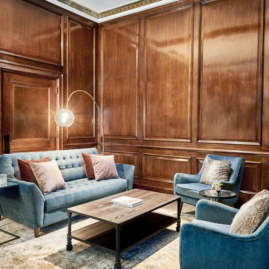 Rich walnut paneling and tufted blue seating create an intimate salon where brass arc lighting casts a warm glow across this sophisticated gathering space.
