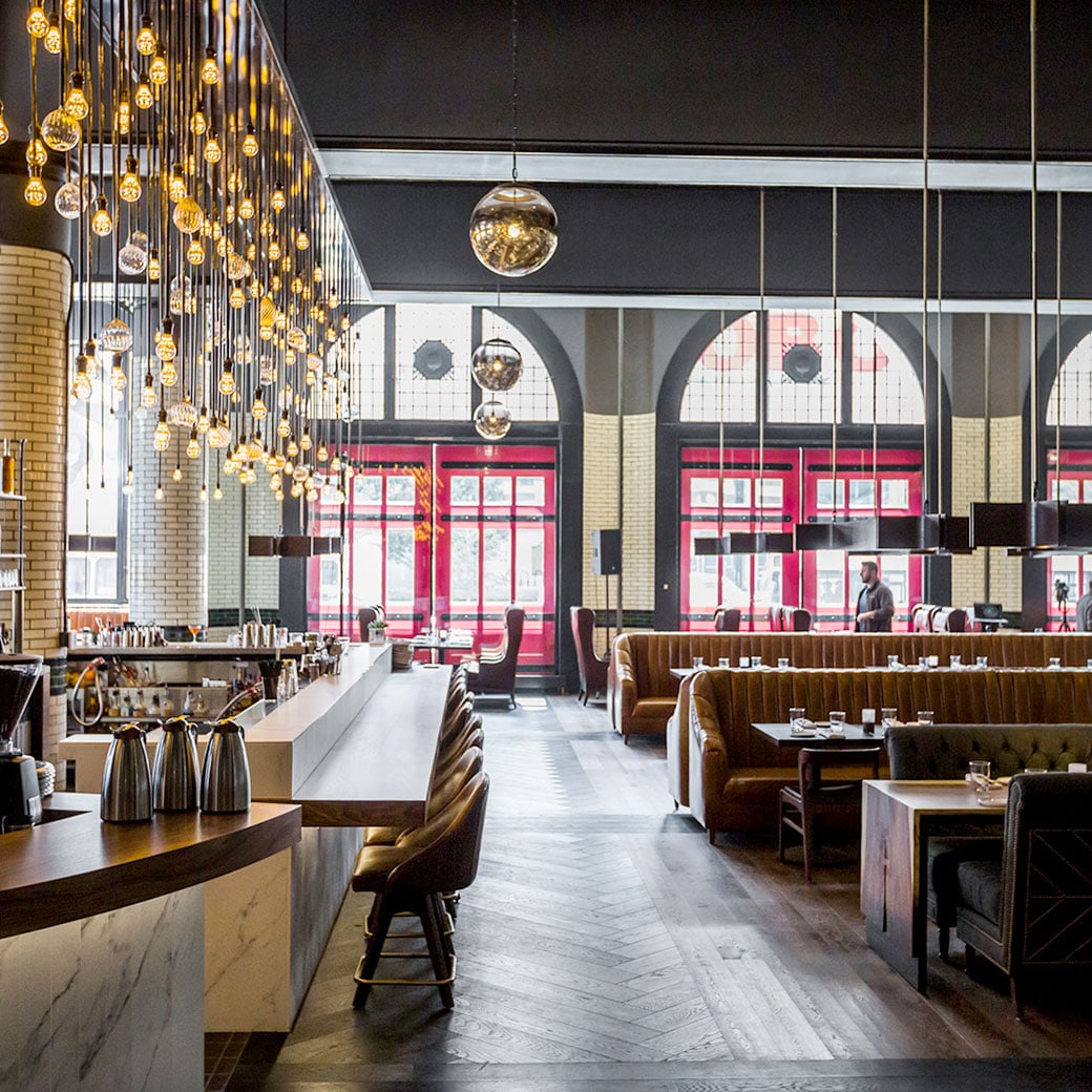 Cascading golden orbs illuminate the hotel's striking restaurant, where cognac leather banquettes and exposed brick create an industrial-chic atmosphere beneath soaring ceilings.